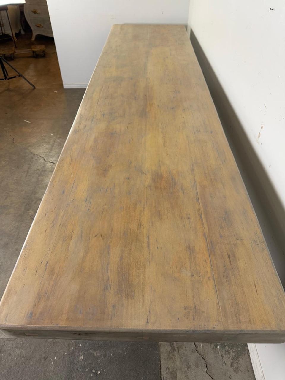 This is a large, rustic-style dining or farmhouse table with a solid wood construction.  The table features a thick, rectangular tabletop with a slightly weathered finish.

The base consists of two substantial pedestal legs, with a stacked,