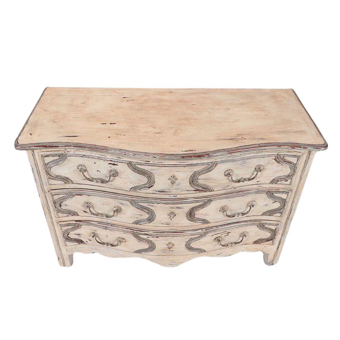 Commode à trois tiroirs vers 1940, de style Regency, peinte en blanc avec des accents bleu-gris.  La commode de style français est soulignée par un gracieux bord festonné au niveau du tablier.