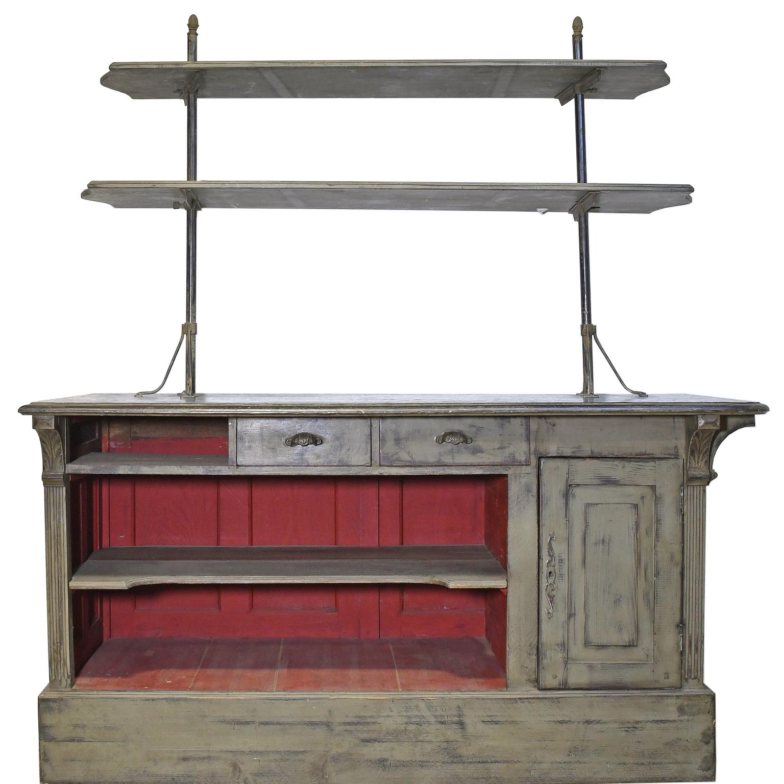 An unusual and beautiful antique shop counter that may have come from a European bakery, with zinc top and panelled front and sides, with carved acanthus on fluted corner pilasters. Two long, adjustable wooden shelves are supported on metal poles