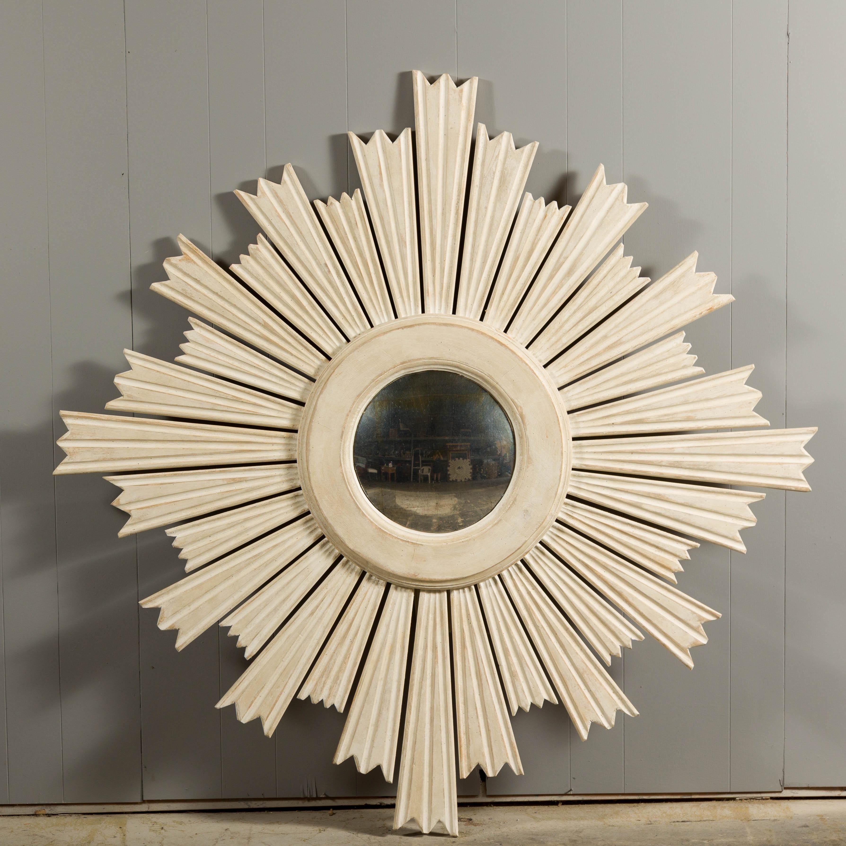 Modern painted wood sunburst mirror with light painted finish, small convex mirror and rays of alternating heights. This modern painted wood sunburst mirror is a striking testament to contemporary design. Crafted with meticulous attention to detail,
