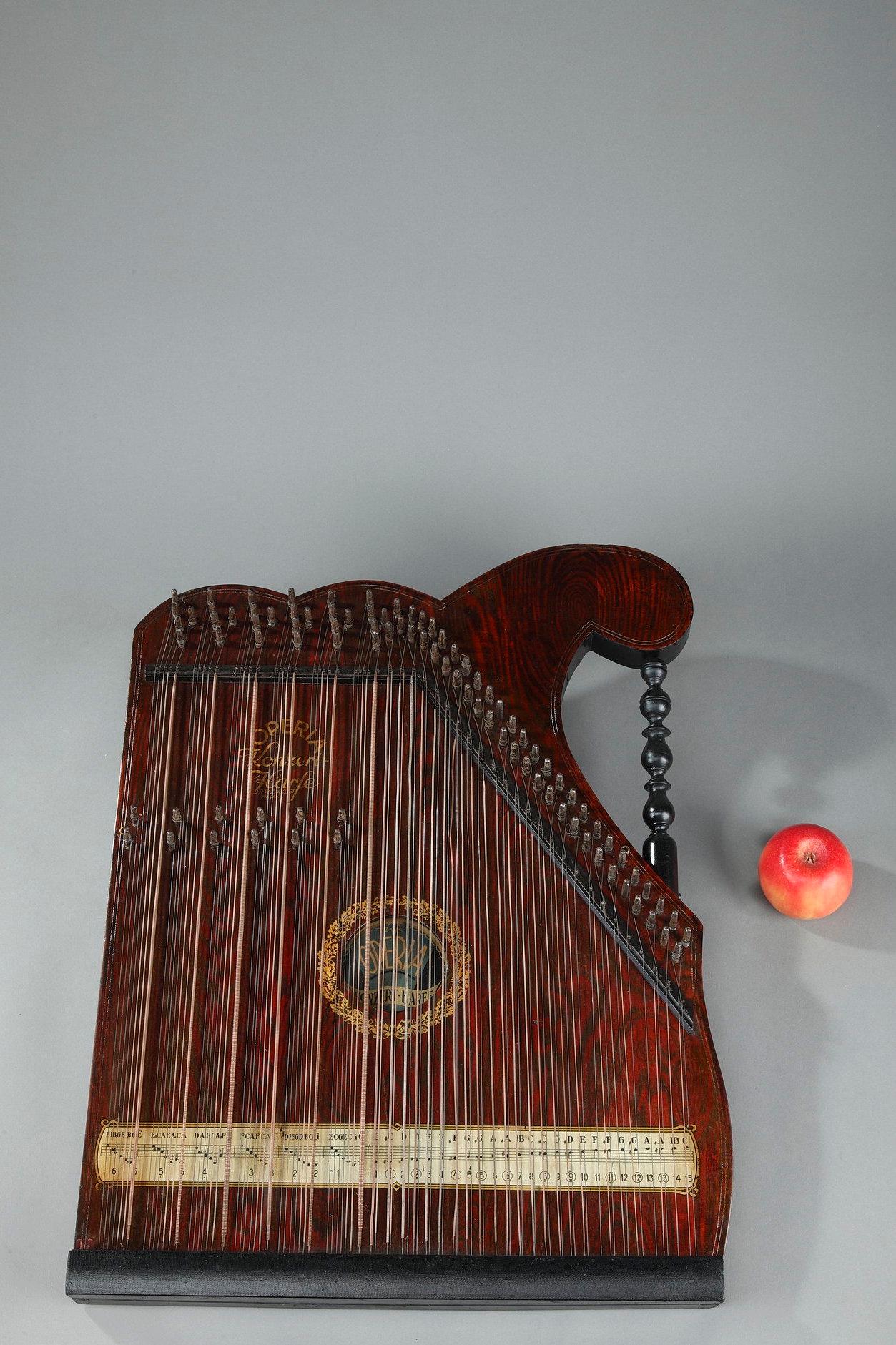Table zither in painted wood. The handle is made of turned blackened wood. The rosette of the resonance box is decorated with a crown of oak leaves. The tablatures are indicated at the bottom of the instrument. The Operia Konzert-Harfe stamp is