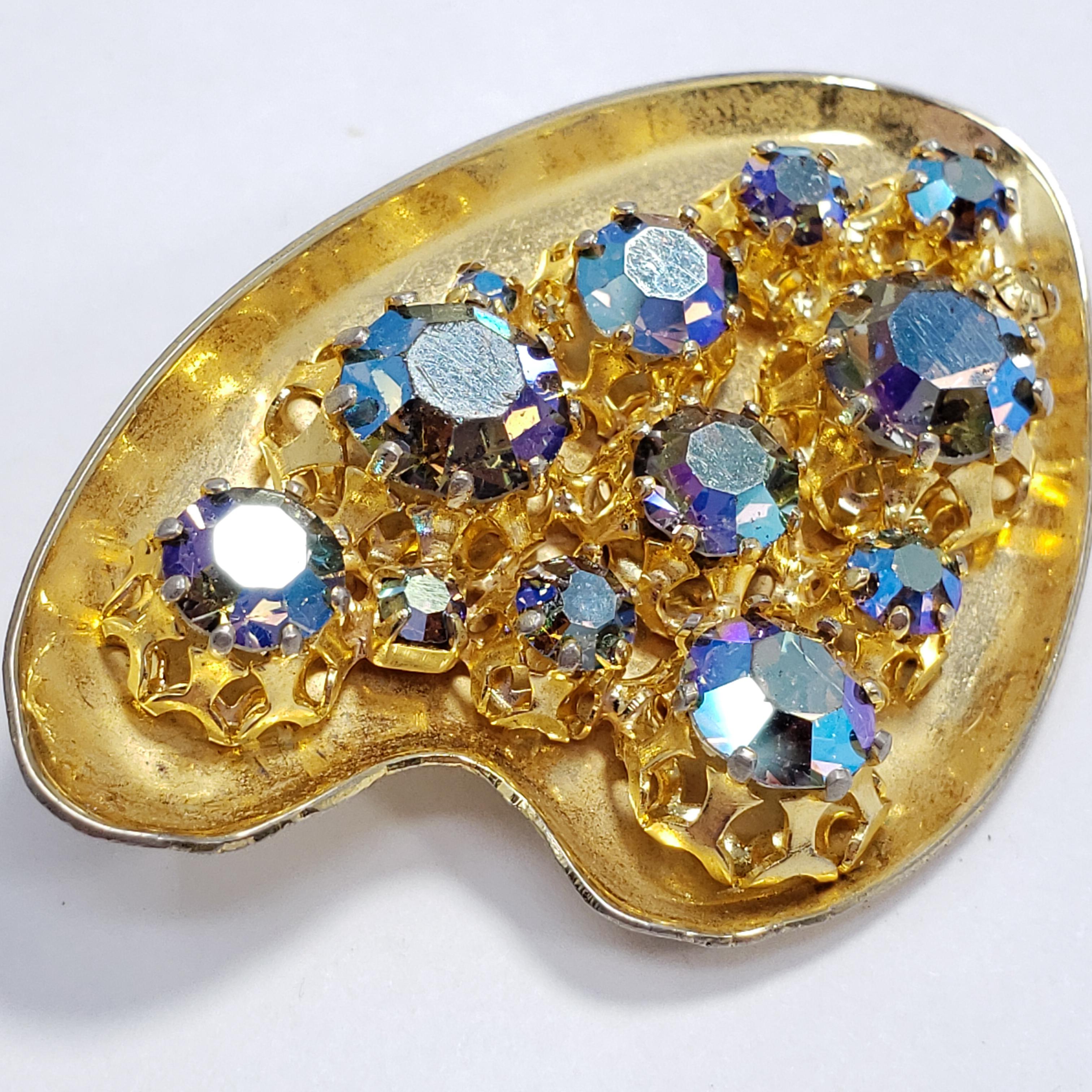 A whimsical pin brooch featuring aurora borealis crystals prong set in a gold-tone, easel-motif setting. Stylish!