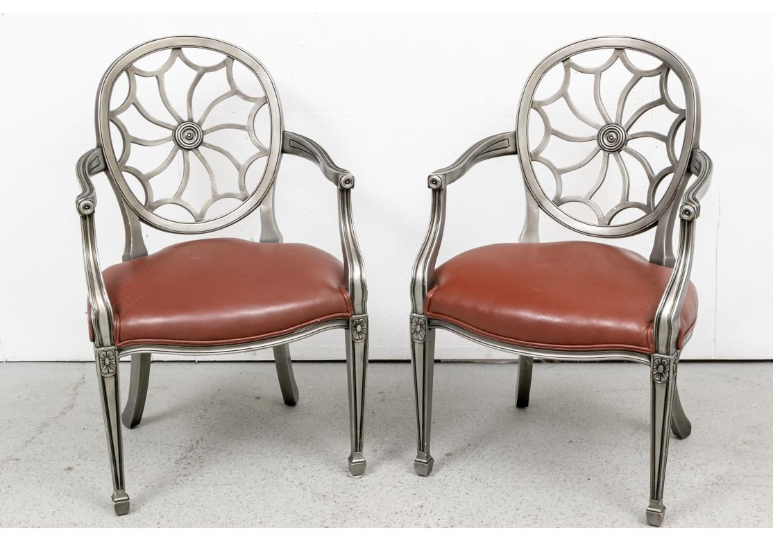 A dramatic pair of Hollywood Regency style Spider Web Armchairs. Carved armchairs in a classic Hollywood Regency style with spider web backs. Carved frames in a gun metal gray finish with brown leatherette seats. Ribbed curved arms and square