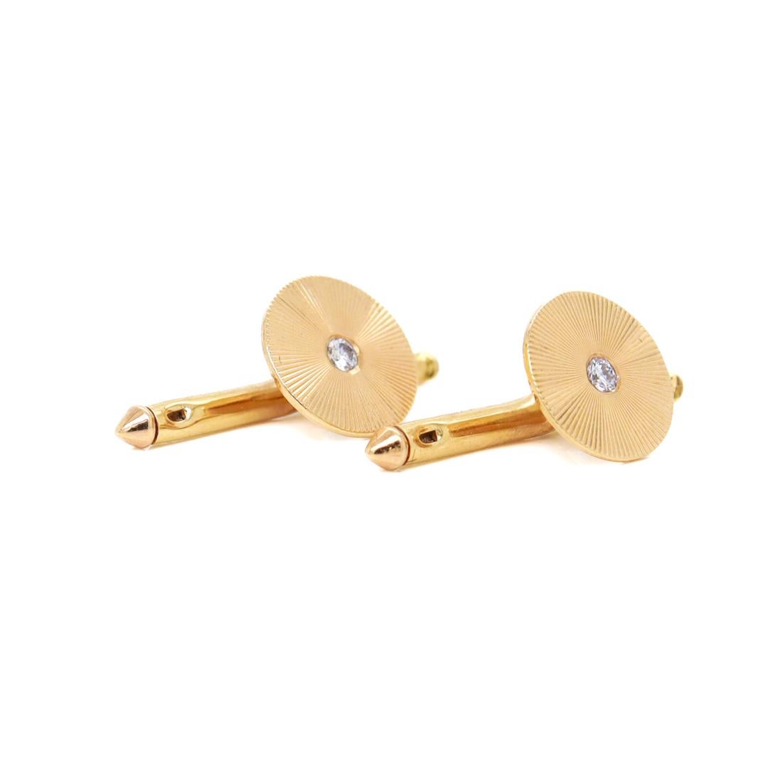 A fine pair of gold & diamond studs or buttons.

By Tiffany & Co.

In 14 karat yellow gold.

Each with a round head and engraved with an starburst pattern centered on a round single cut white diamond.

The engraving catches and reflects light in a