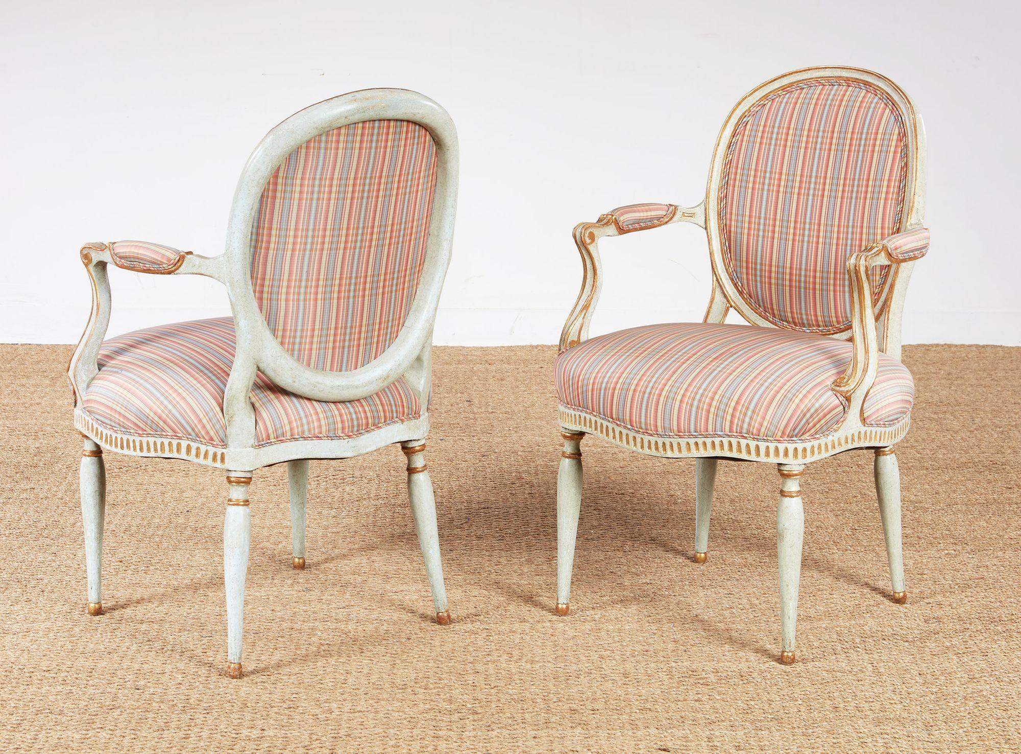 A pair of 18th century Georgian painted and gilt armchairs with upholstered balloon backs, padded arms and upholstered seats on shaped and carved aprons, on turned legs, with gray painted and gilt detailed surface.  