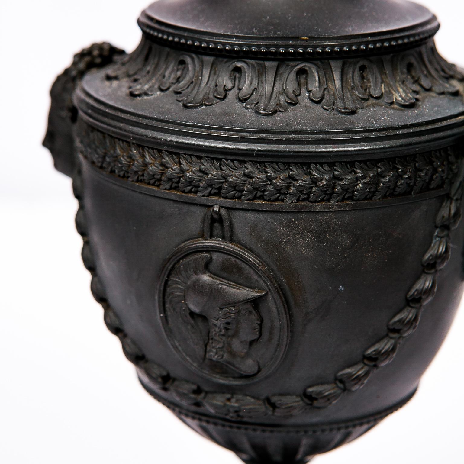 A pair of Black Basalt covered urns made by H. Palmer of Hanley Staffordshire.
This pair of vases is a gem of the neoclassical style. They combine beautiful molded Athena Cameos, exceptional Cleopatra mask handles supported by swags of husk, with