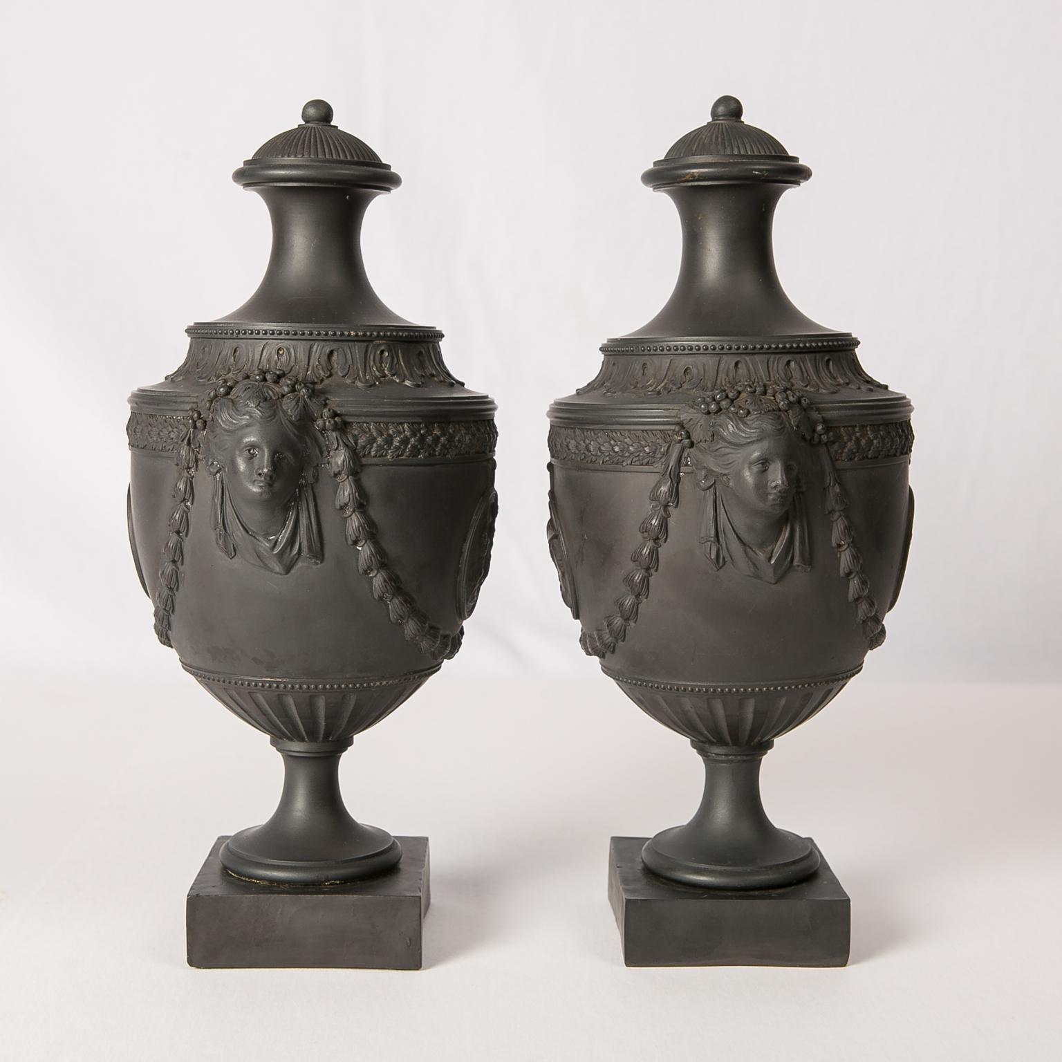A pair of Black Basalt covered urns made by H. Palmer of Hanley Staffordshire in the 18th century, circa 1775. 
This pair of vases is a gem of the neoclassical style. They combine beautiful molded cameos, and exceptional Cleopatra mask handles