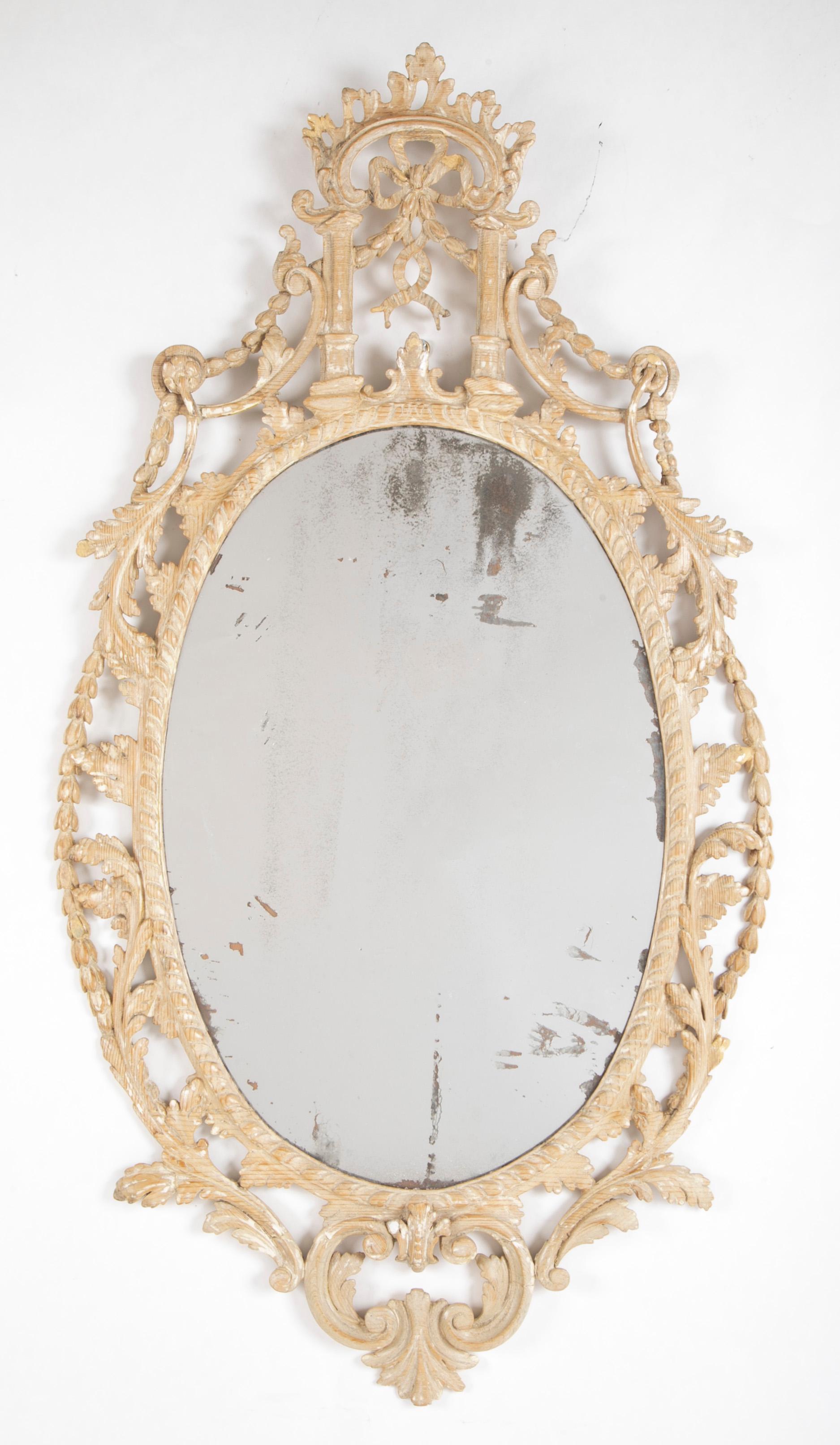 Very fine and elegant pair of carved pine Adam Style oval mirrors. Detailed and delicate acanthus and floral carving throughout. Each crowned with a pair of columns supporting an arch with exquisitely carved bow, with a bell flower garland. The pine
