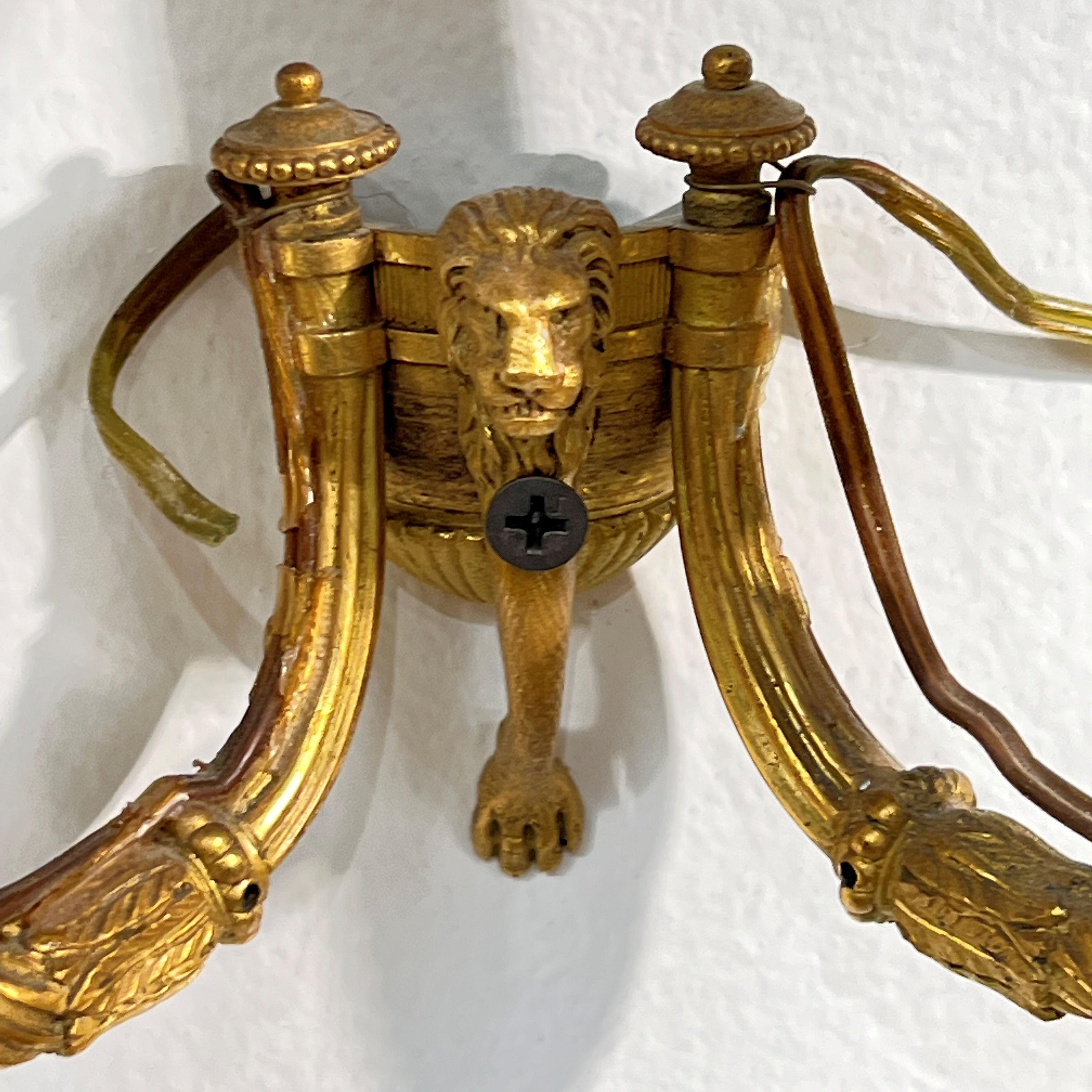 Our pair of ormolu bronze wall lights from the late Georgian period date from the late 18th century. They feature two u-shaped candle arms decorated with an acanthus leaf and bellflower motifs, emanating from wall plates with mask, leg and paw of a