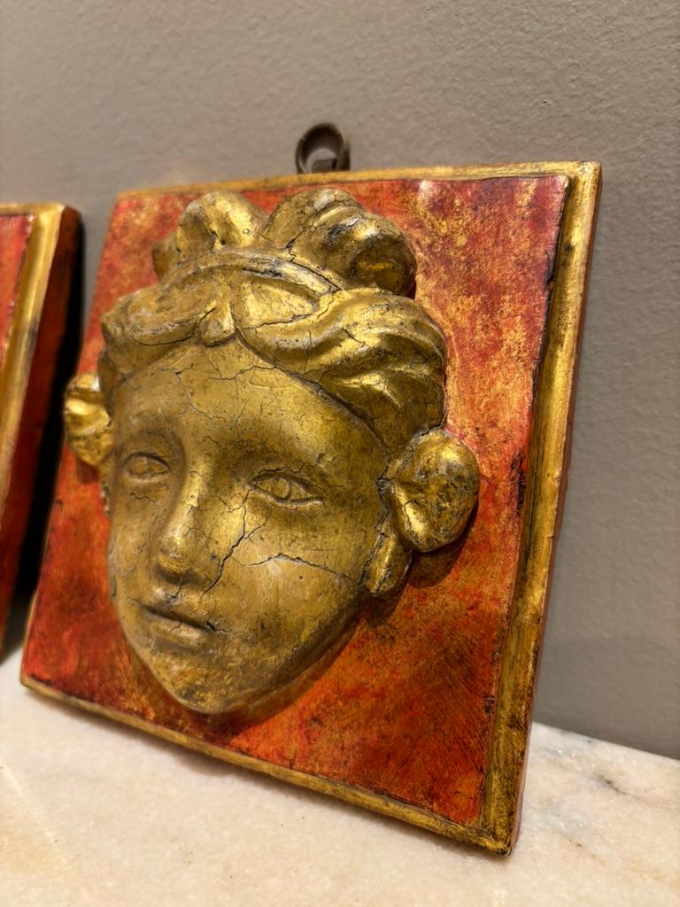 Pair 18th Century Italian Neoclassical hand carved giltwood and red paint masks in high relief. each showing a female goddess with a diadem in her hair and serene facial expression. The gilded heads carved in deep relief on a rectangle framed with