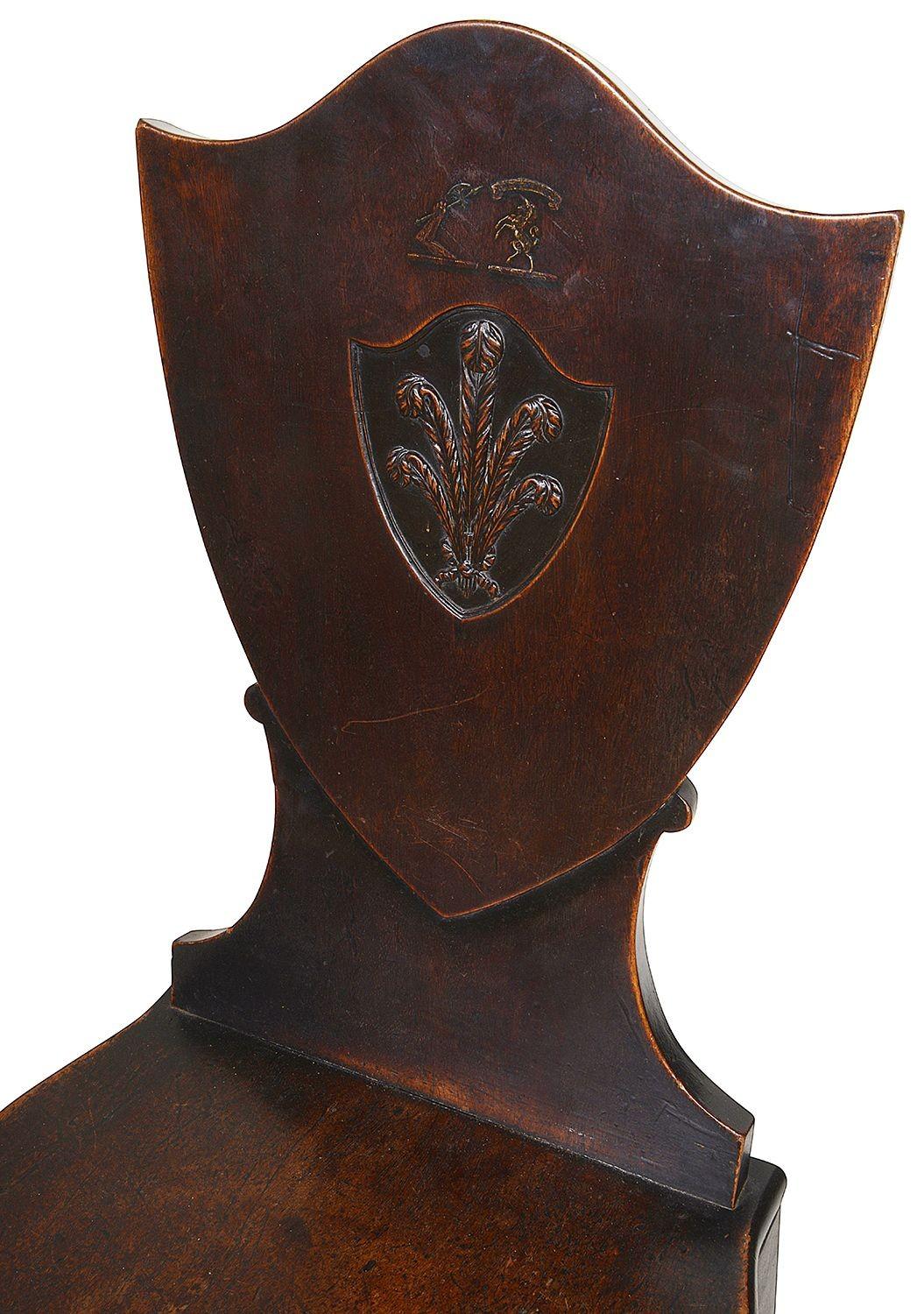 A good quality pair of 18th century mahogany hall chairs, each with sheild back and an inset panel depicting a painted armorial above a carved wood Prince of Wales ploom. Wooden seats raised on square tapering legs, circa 1780.

Batch 67 61040
