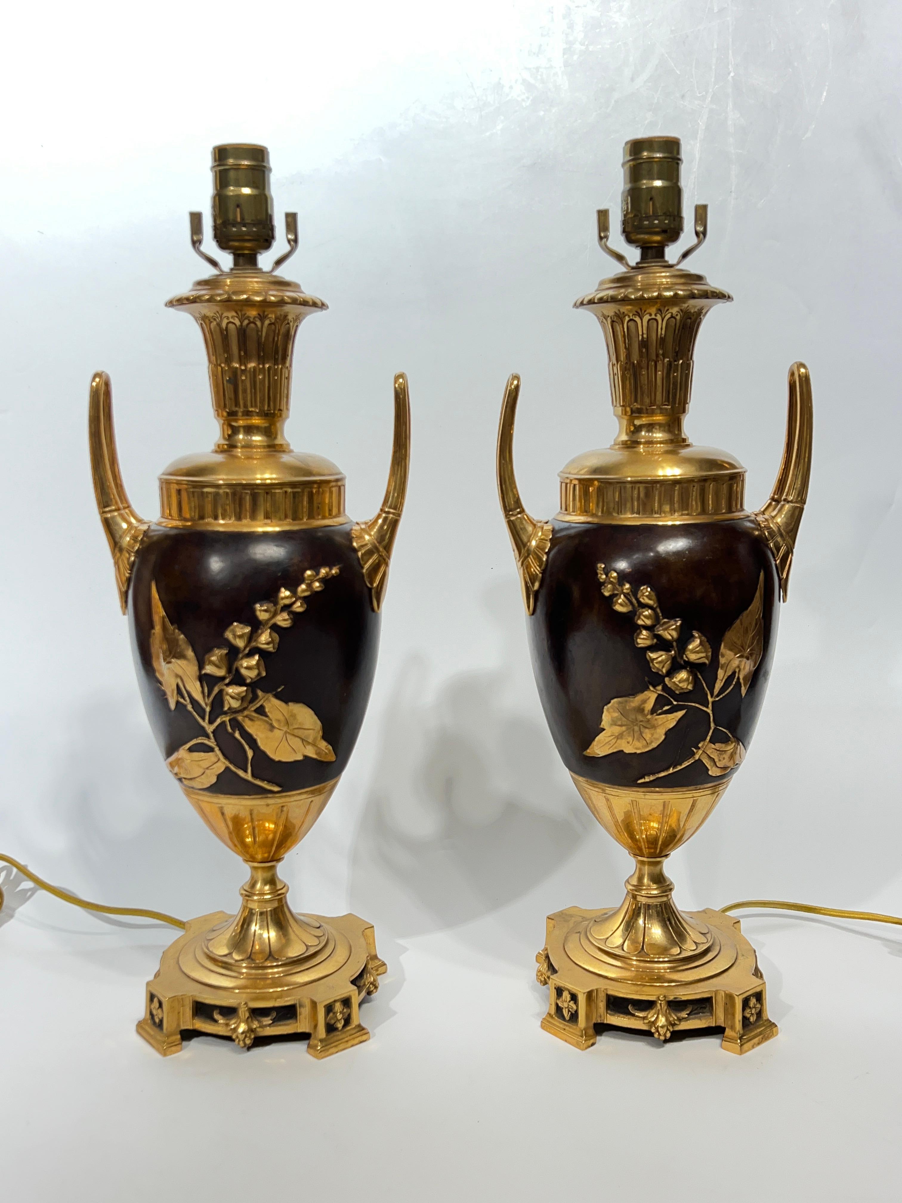 Pair of gilt and patinated and git  bronze table lamps with urn shape with looping handles and raised gilt designs of blooming tree branches.