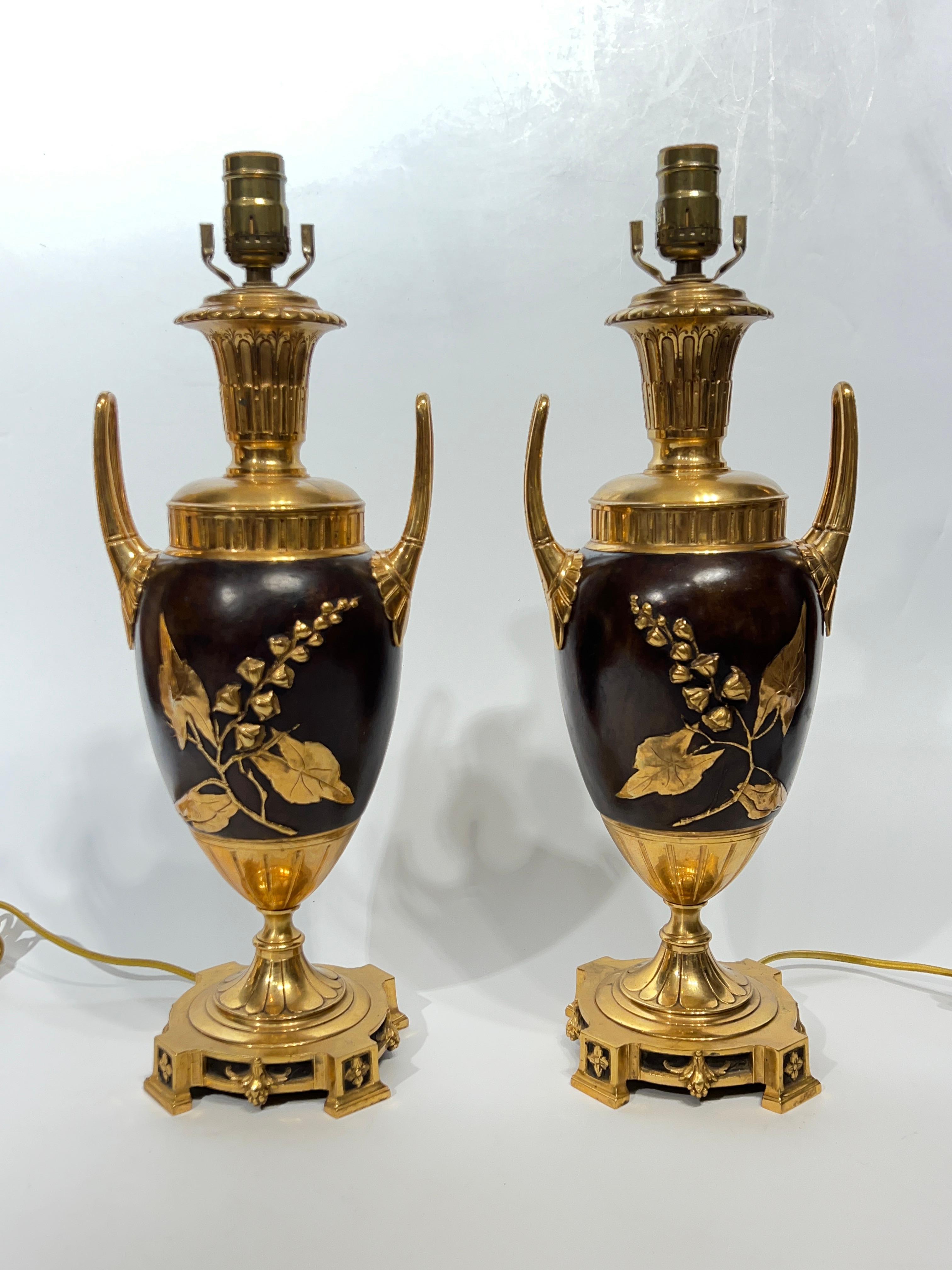 Paire d'objets en métal doré, patiné et git  Lampes de table en bronze en forme d'urne avec des poignées en boucle et des motifs en relief dorés de branches d'arbres en fleurs.