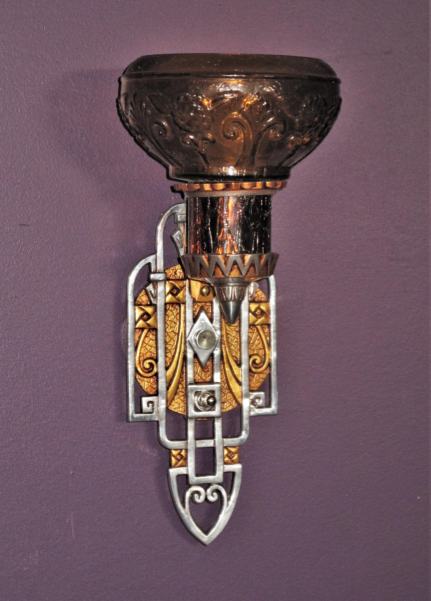 One of the more unique pair of sconces from the period when both Art Deco and Spanish Revival were popular design elements, most likely form the late 20s. Lots of deco inspired designs on the back plate and a Revival inspired glass shade and shade