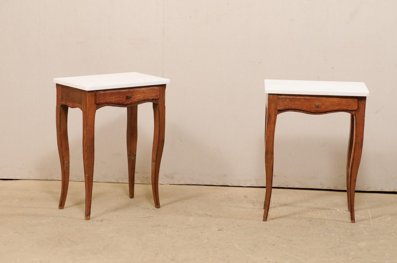 A French pair of side tables from the 1920s with new quartz stone tops. These antique tables from France each have a single drawer housed within the delicately scallop-carved skirt and are raised upon four gracefully curved legs which taper gently