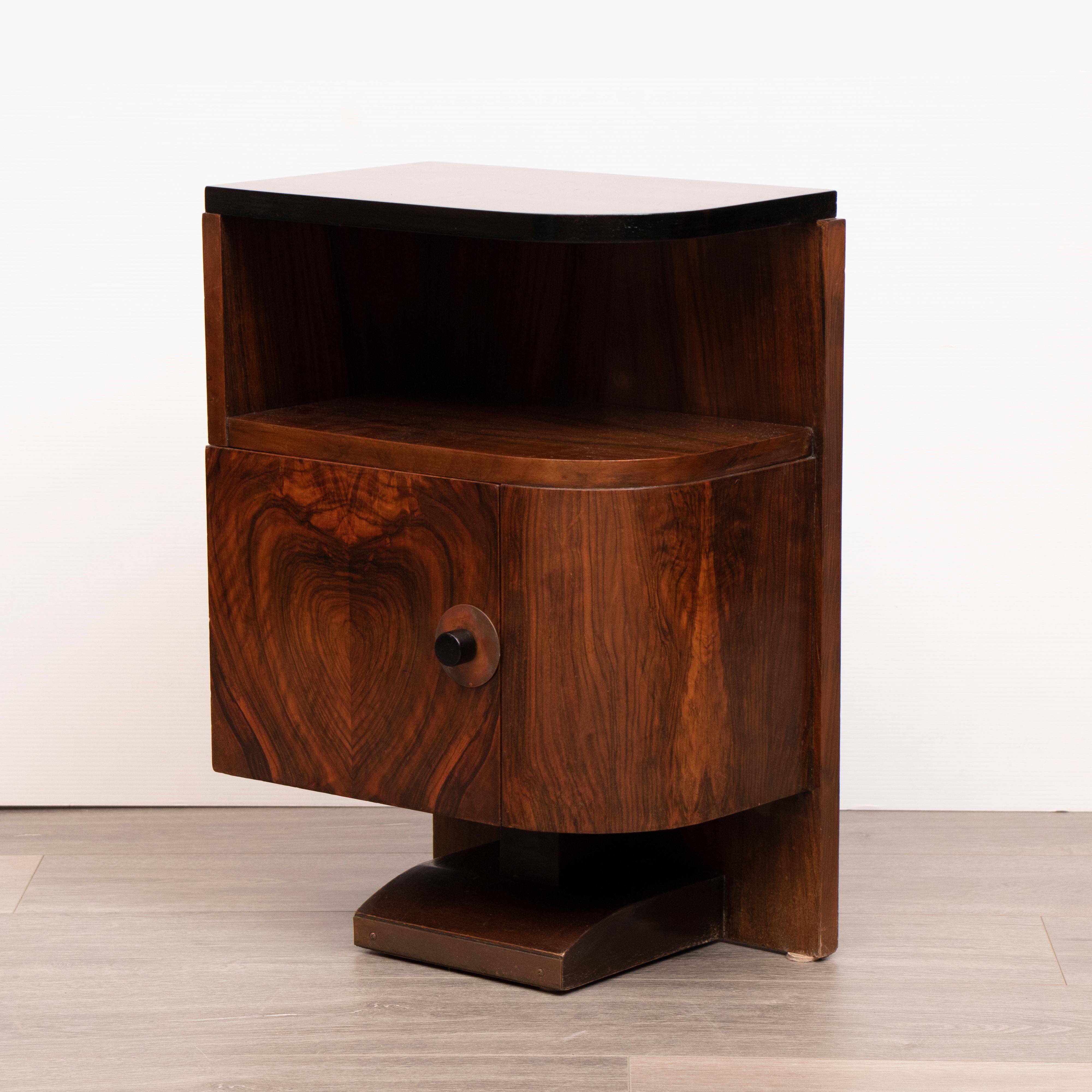 A pair of French 1930s Art Deco Walnut bedside tables or nightstands. The tops of each table have recently been refinished with a black lacquer paint. A space sits beneath each top where magazines can be stored. A single door opens on each cabinet
