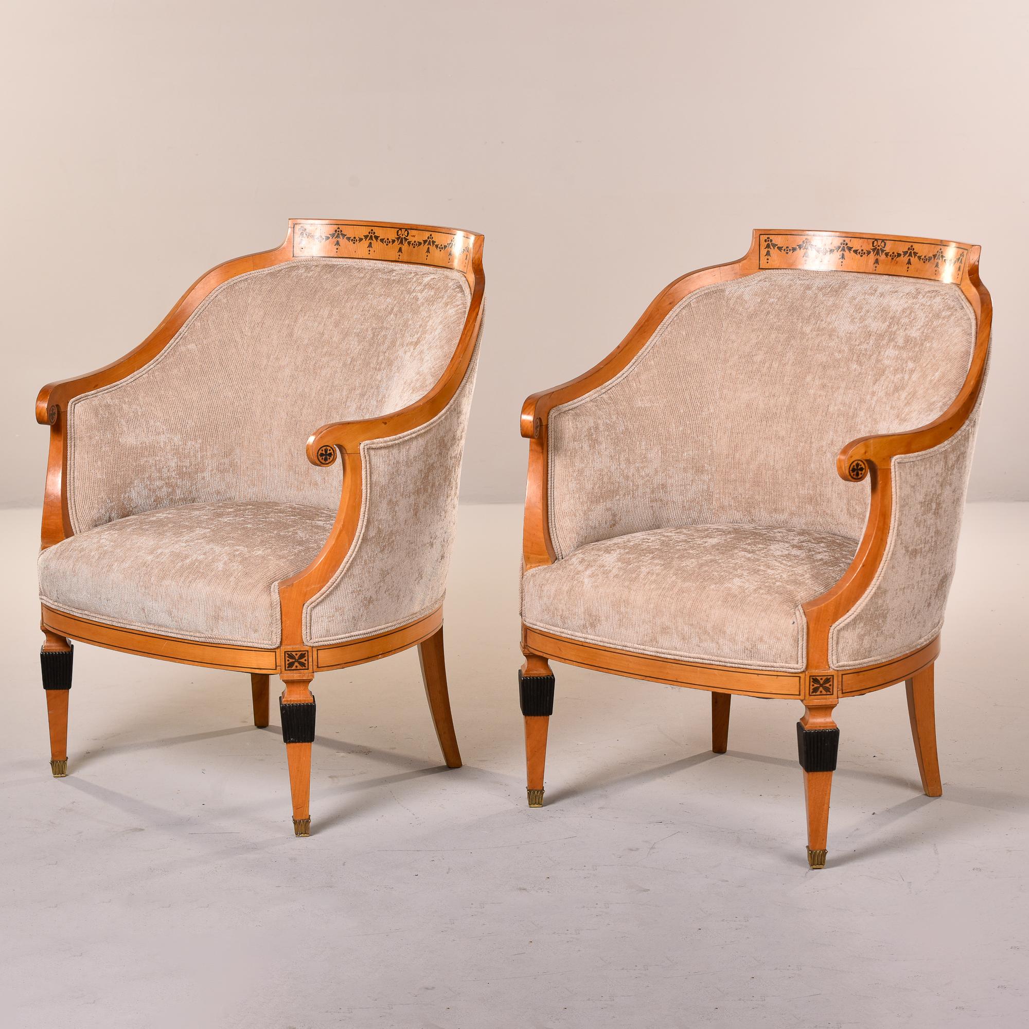 Found in France, this pair of circa 1930s Bergere chairs have light wood frames with curved seat backs and curved arms. Frames have painted floral details on top of seat backs, outside of arms and painted medallions at top of front legs. Front legs