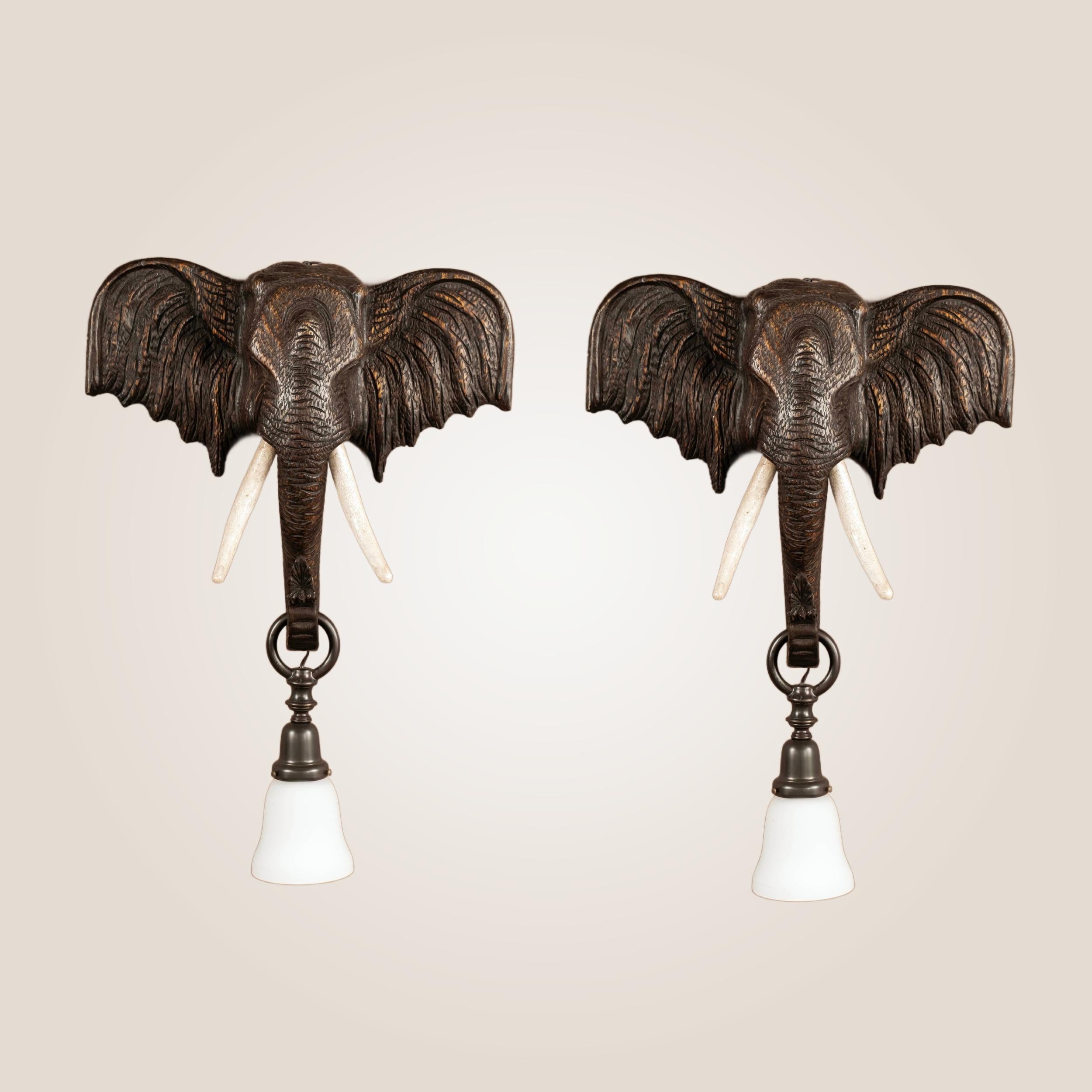Pair of 1940s Continental elephant head sconces featuring flared ears, and the trunk carrying a white glass lantern.