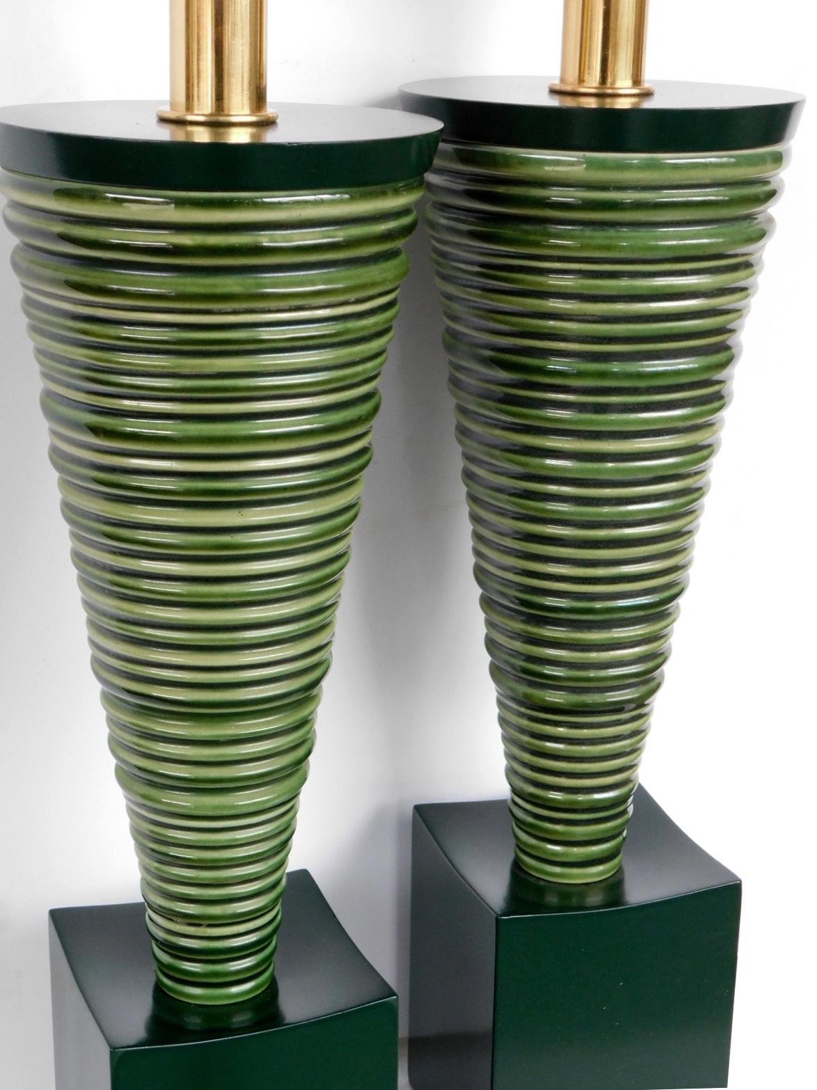 Great midcentury design, each ribbed conical-shaped ceramic lamp resting on a concave forest-green lacquered wooden plinth; Measures: 17