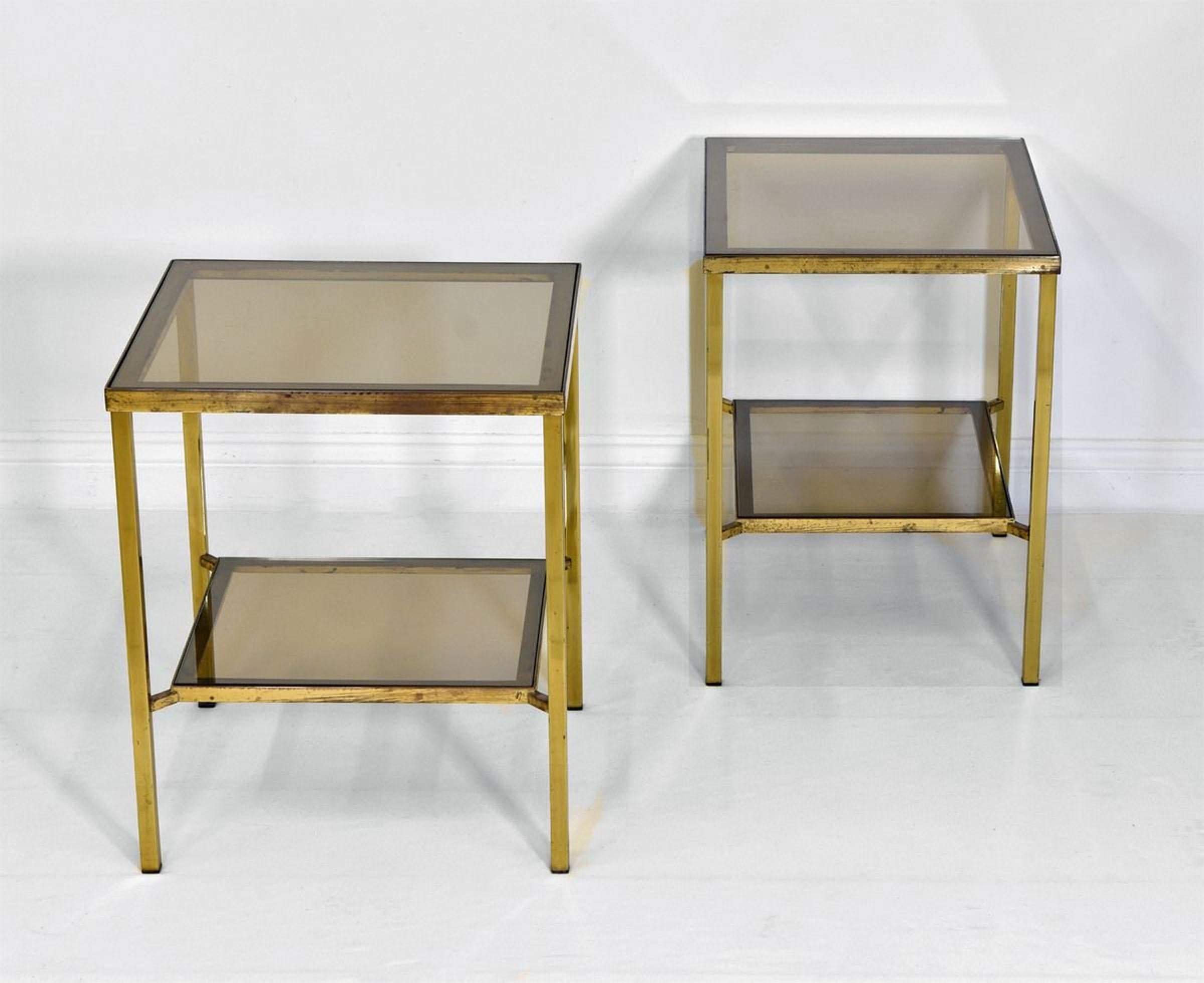 A matching pair of vintage brass side tables with two tier lightly smoked glass insets. Probably French. Circa 1970.

The tables' brass angular frames have the natural ageing and patina as befitting their age. The feet caps are all intact.

One