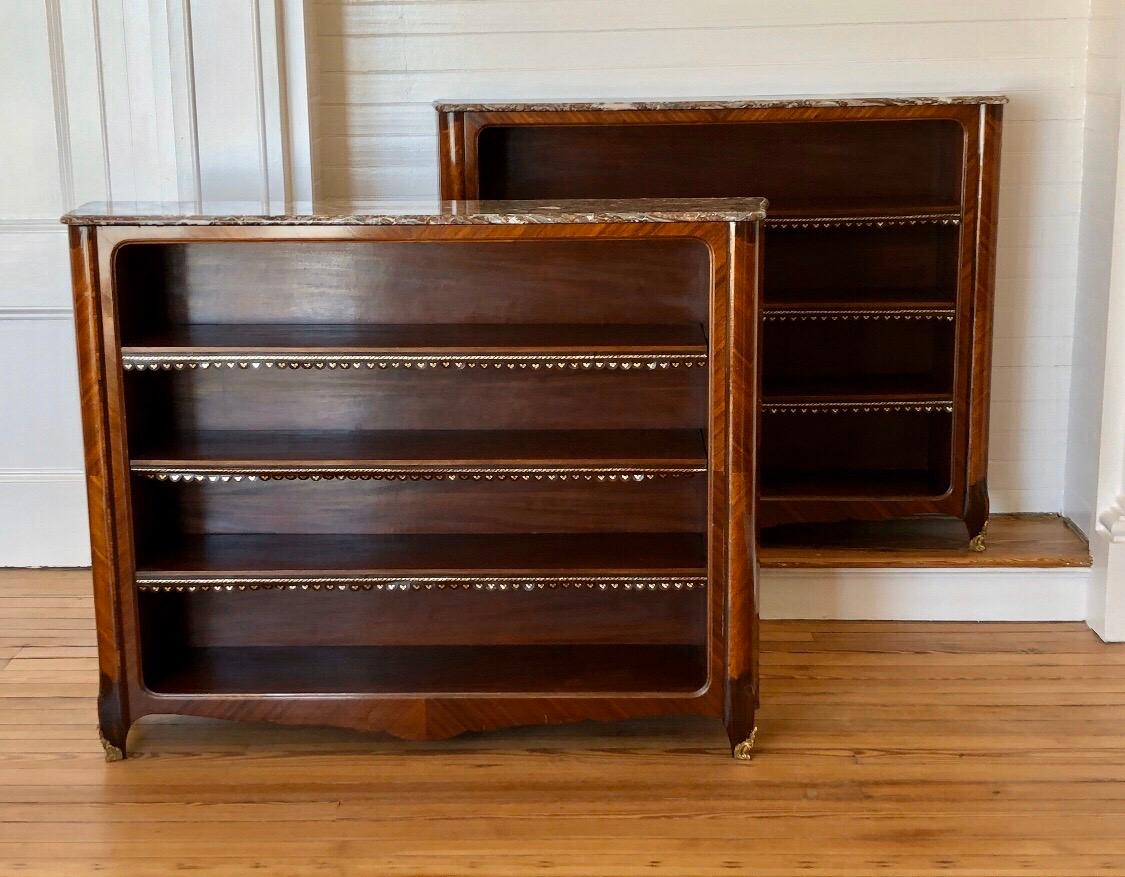 A Regal pair of Louis XV style French ormolu-mounted marble top Bibliotheques with rosewood, Kingwood, Tulipwood, and mahogany veneers. These elegant French bookcases showcase the refined craftsmanship of the Ebénistes work with the use of rich