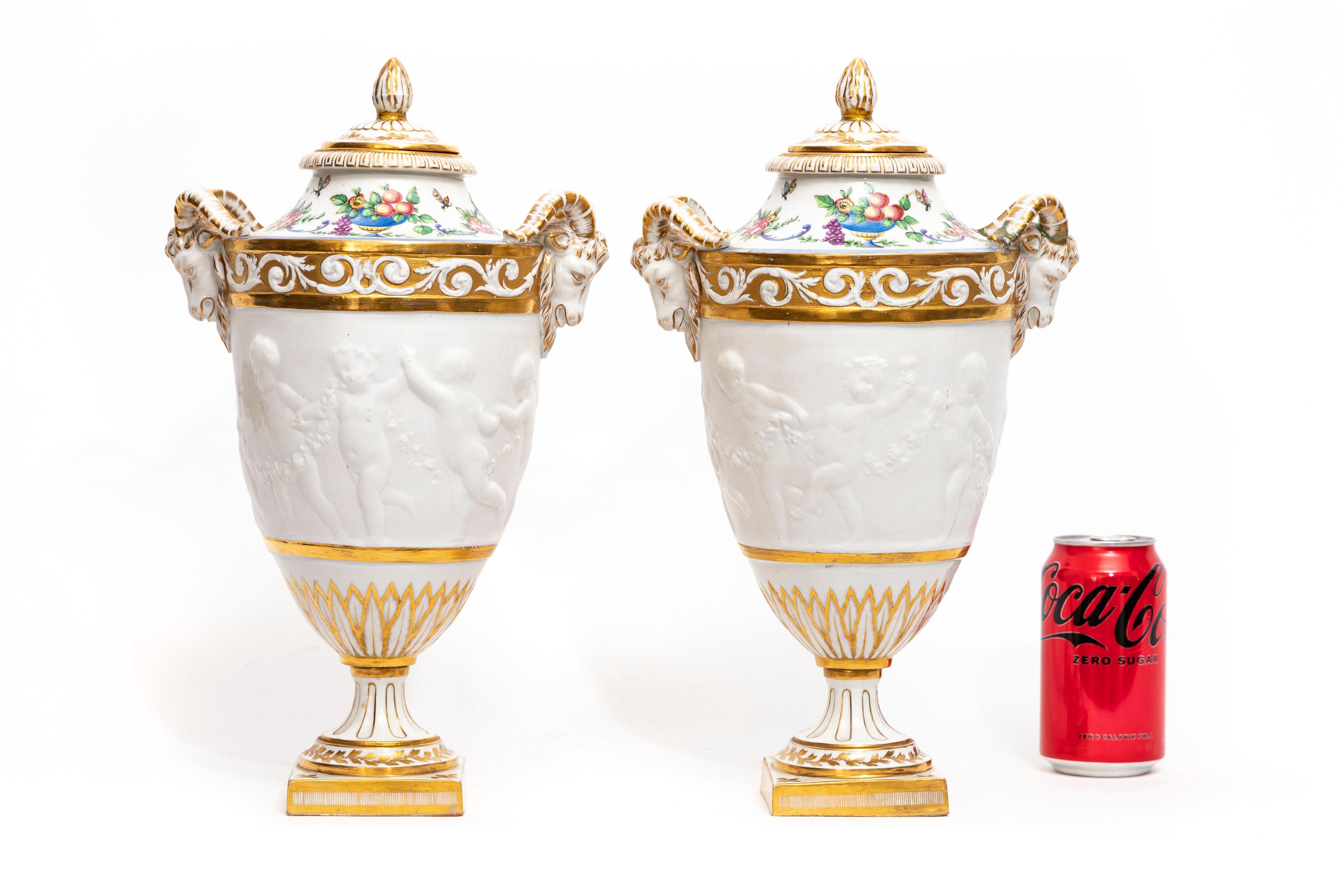 A Magnificent Pair of 19th Century French Sevres Biscuit Porcelain Lidded Vases with Rams Head Handles and 360 Degree Dancing Putti Decoration.  Each vase is finely hand-carved by the finest Sevres makers.  The center decoration is finished with 360