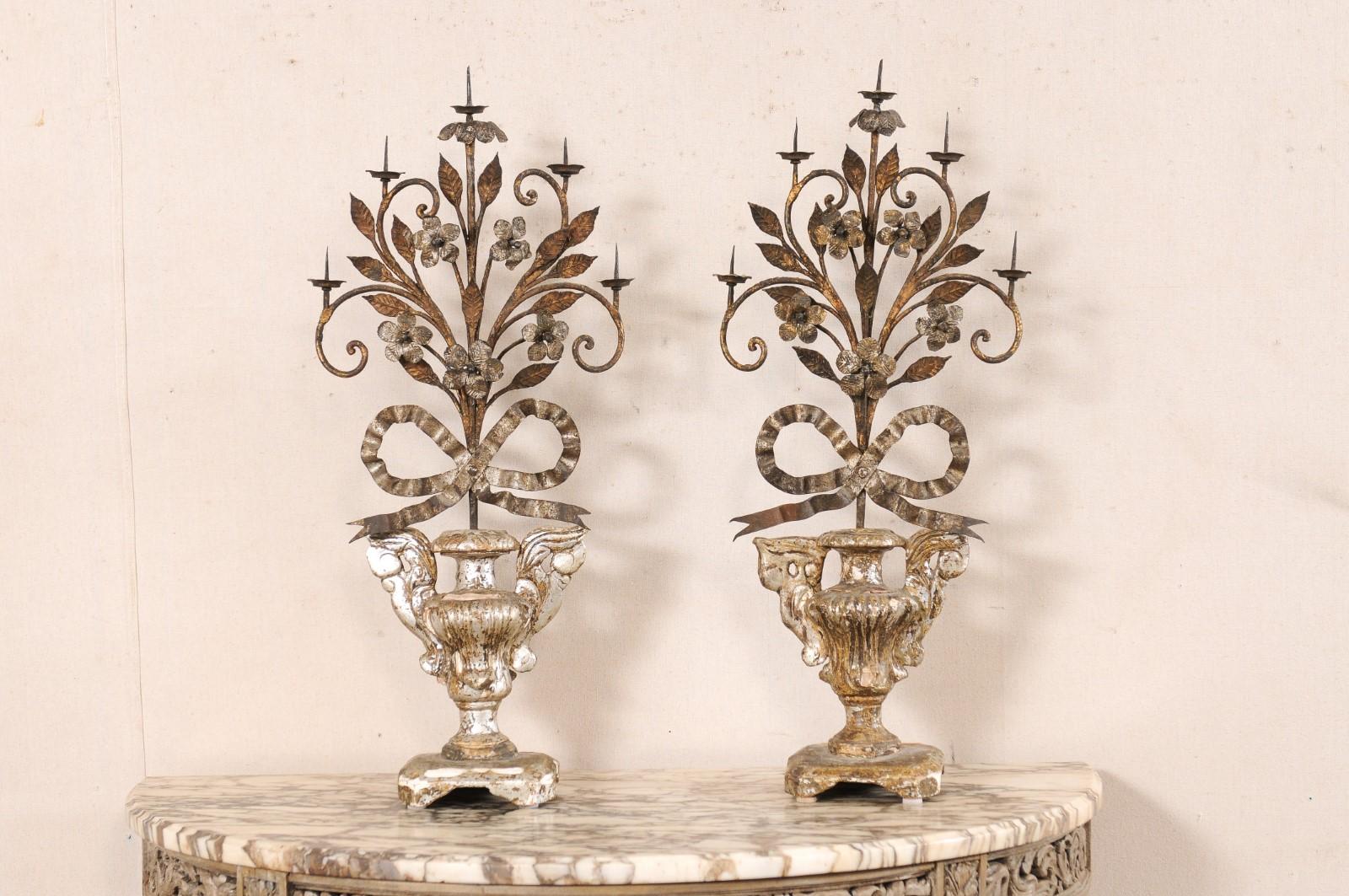 An Italian pair of Neoclassical style five light candelabras from the 19th century. These antique candle holders from Italy are have gesso and silvered/gilt over a carved wood base in a two-handled urn motif, with a ribbon-tied bouquet of metal