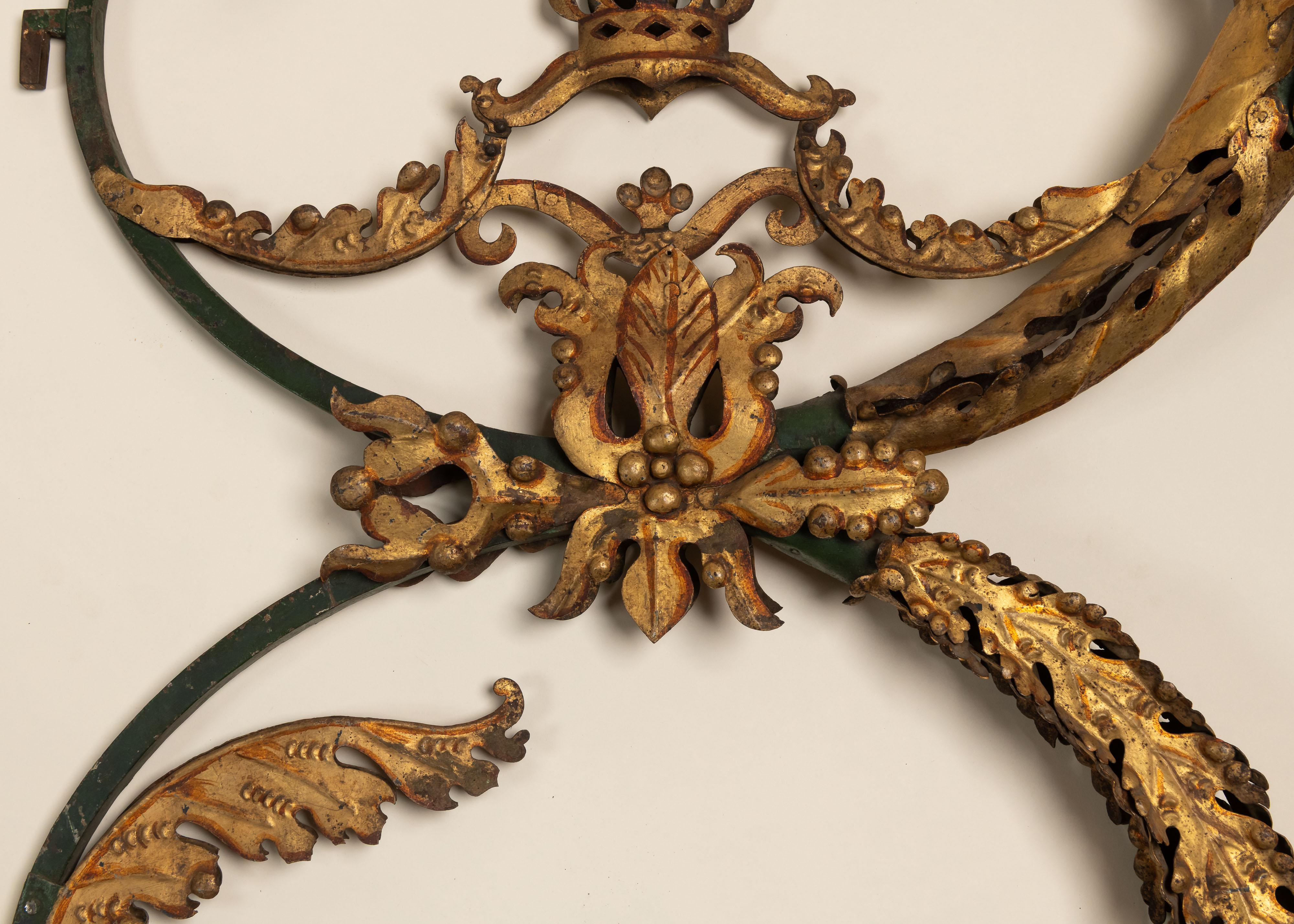 These ornate 18th-century wall sconces are crafted from carved and painted wood with traces of original gilding. Shaped like a curling cornucopia, they feature lush acanthus leaves, floral motifs, and a central crown finial, suggesting aristocratic