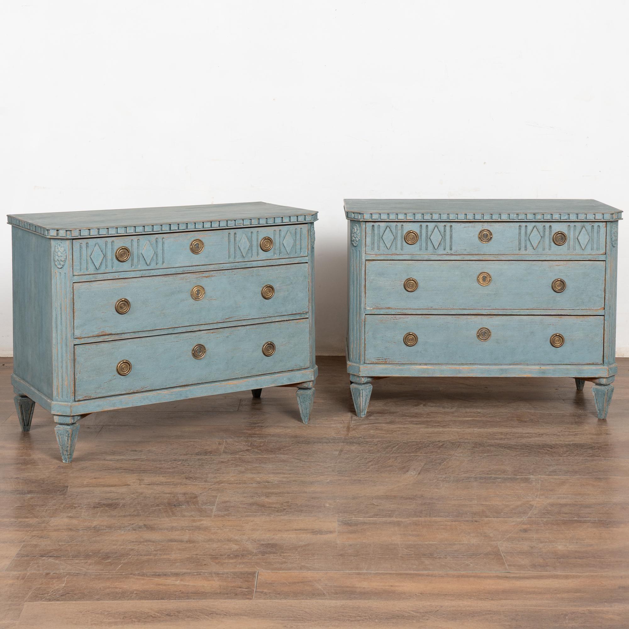 Paire d'élégantes commodes en pin de style gustavien avec des poignées en laiton sur chaque tiroir.
Trois tiroirs, le tiroir supérieur étant décoré de lignes verticales simples et de losanges. Montants latéraux cannelés, moulure en denticule, le