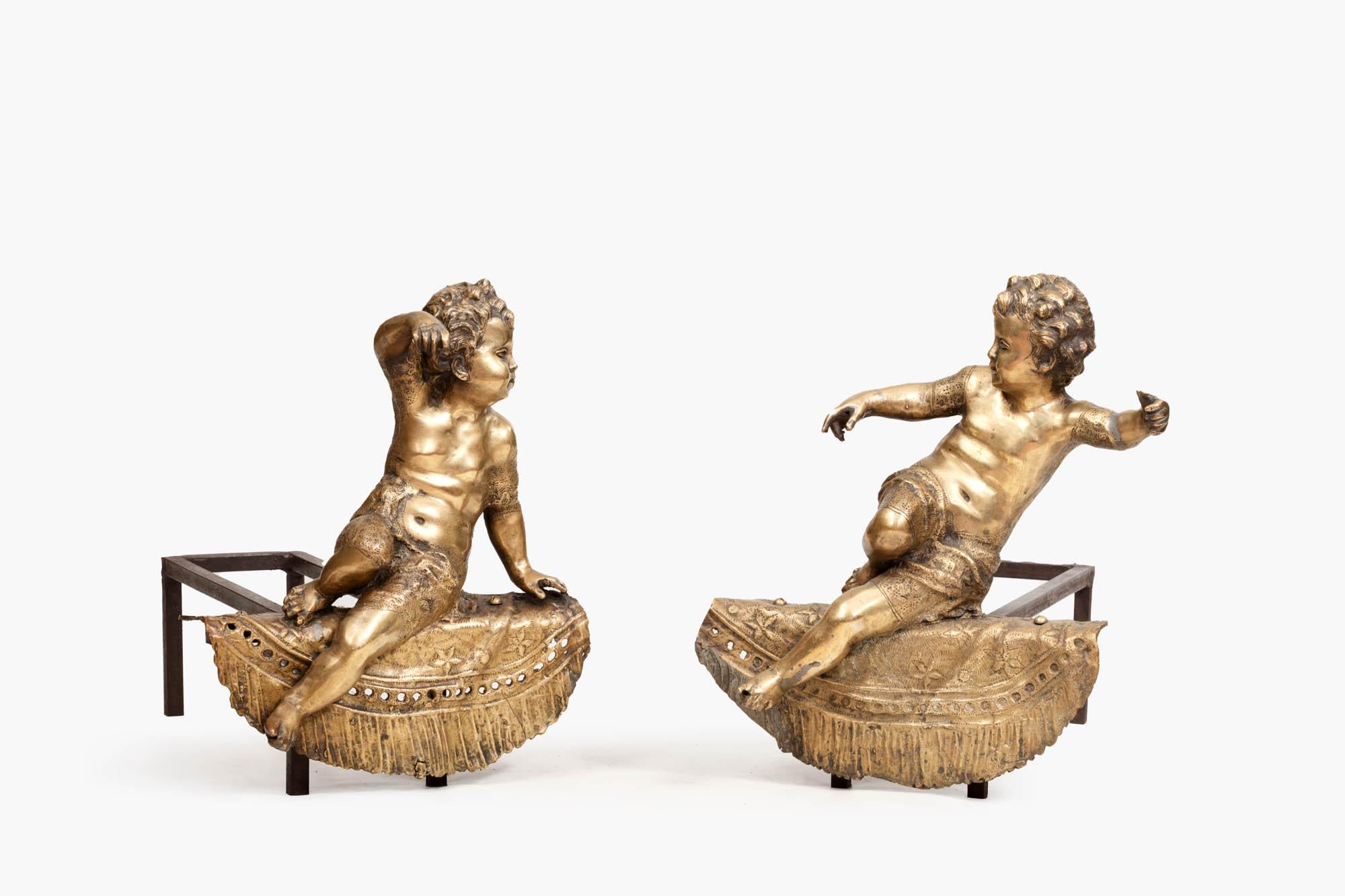 Pair of 19th Century brass fire dogs in the Louis XV style modeled as seated cherubs with outstretched arms. Each sits on a semicircular shelf with fringed and pierced drapery detailing, circa 1880.