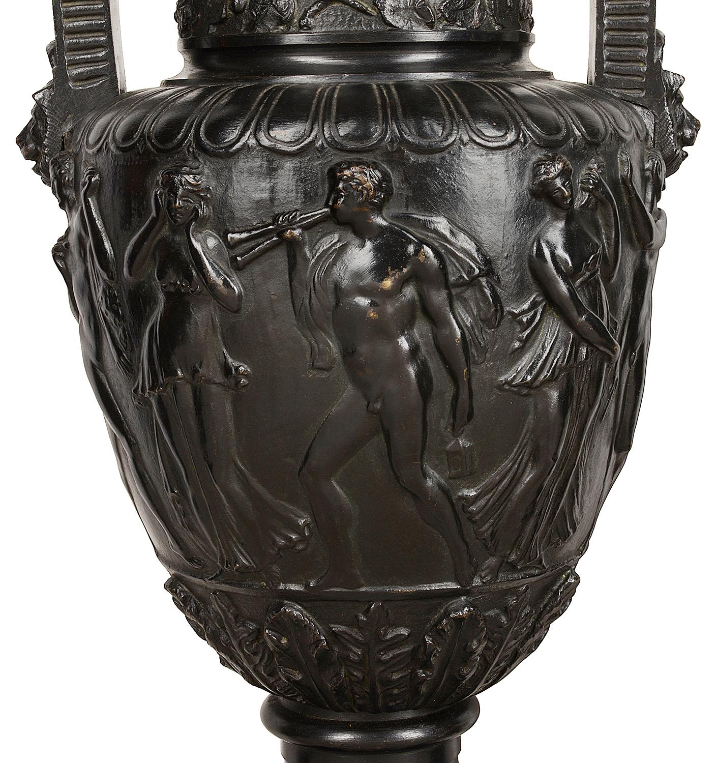 A good quality pair of 19th century French bronze neoclassical two handled lion mask urns, each depicting dancing nude figures around the center and raised on black marble bases with scrolling bronze feet. Measures: 45cm (18.5