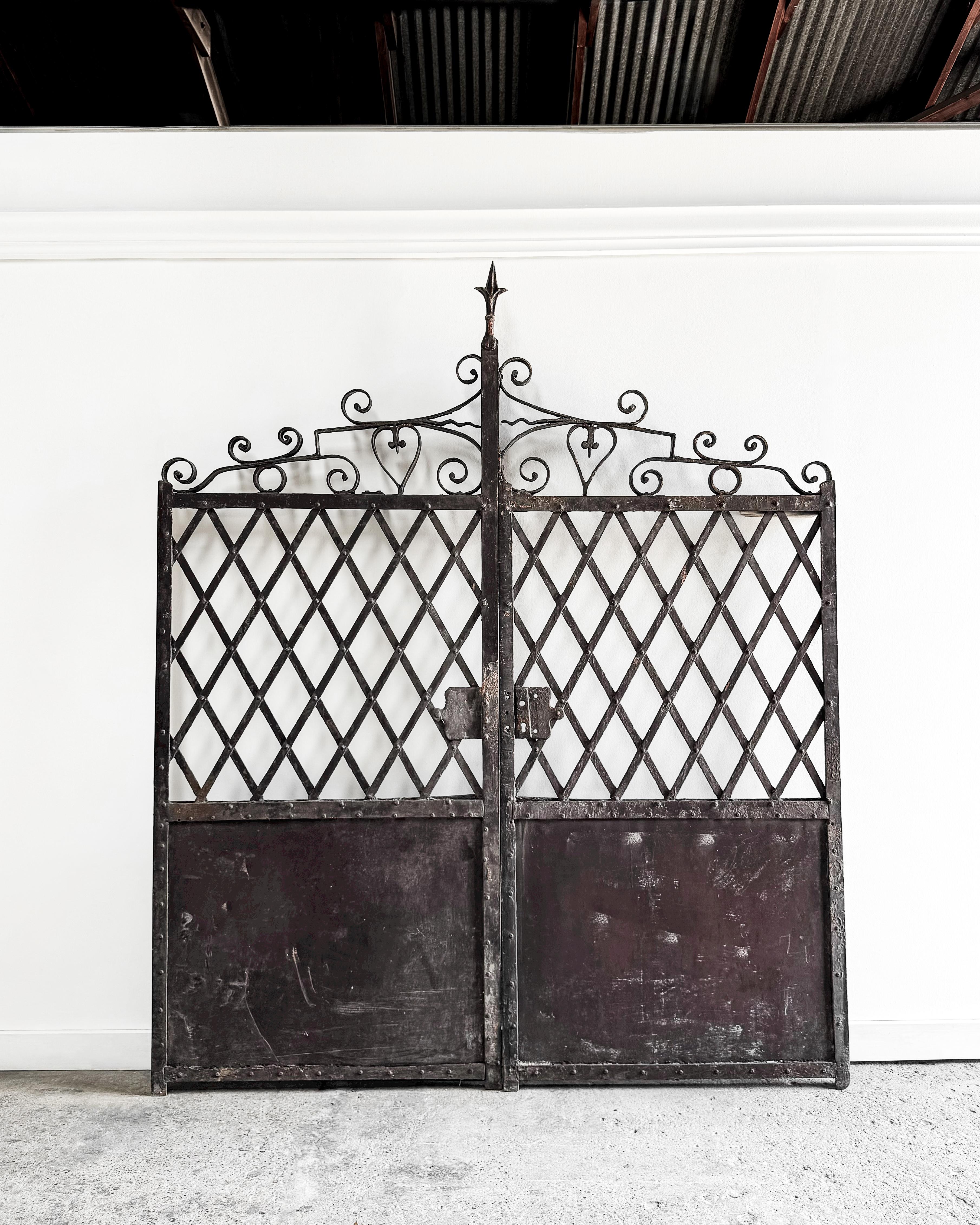 A stunning pair of 19th-century cast iron garden gates showcasing a blend of artistry and durability. The gates feature a distinctive design with an upper section adorned in an X-weave pattern, adding a textured charm to their appearance. Below,