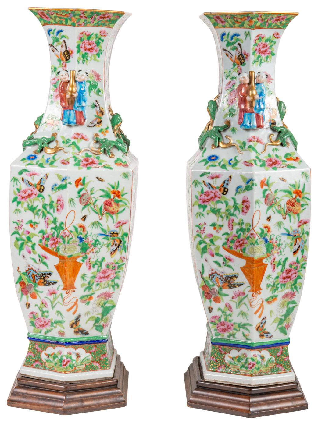 A very good quality pair of mid-19th century Chinese Canton / Rose medallion vases on stands. Each with a white ground, green foliate decoration with exotic bids, flowers and butterflies. Inset panted panels, handles either side of two men carrying