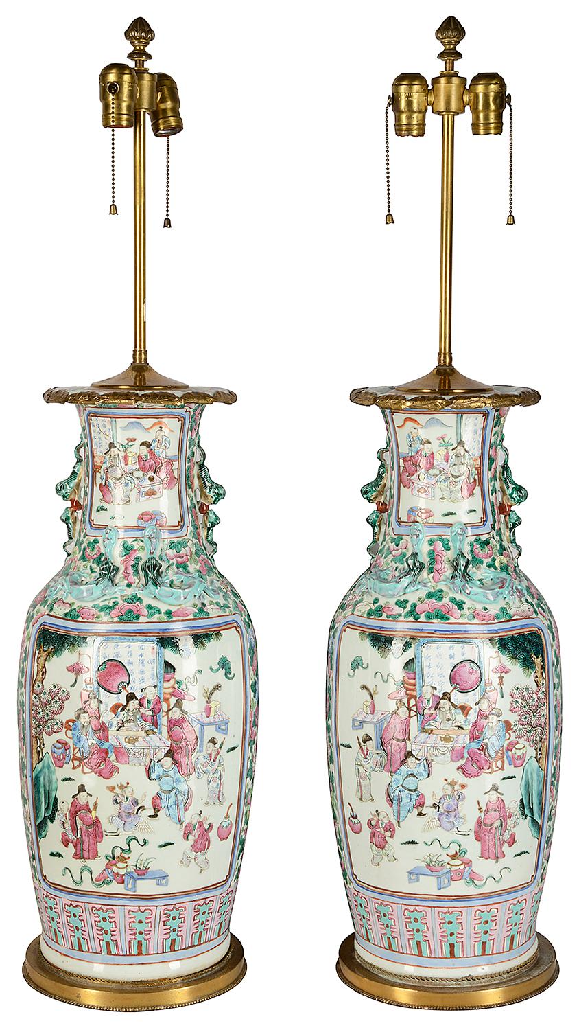 A large pair of Chinese famille rose vases / lamps each with a pink and blue ground, dog of faux handles to either side, ormolu leaf decoration to the rims, inset painted panels depicting classical Chinese scenes of courtiers attendants and