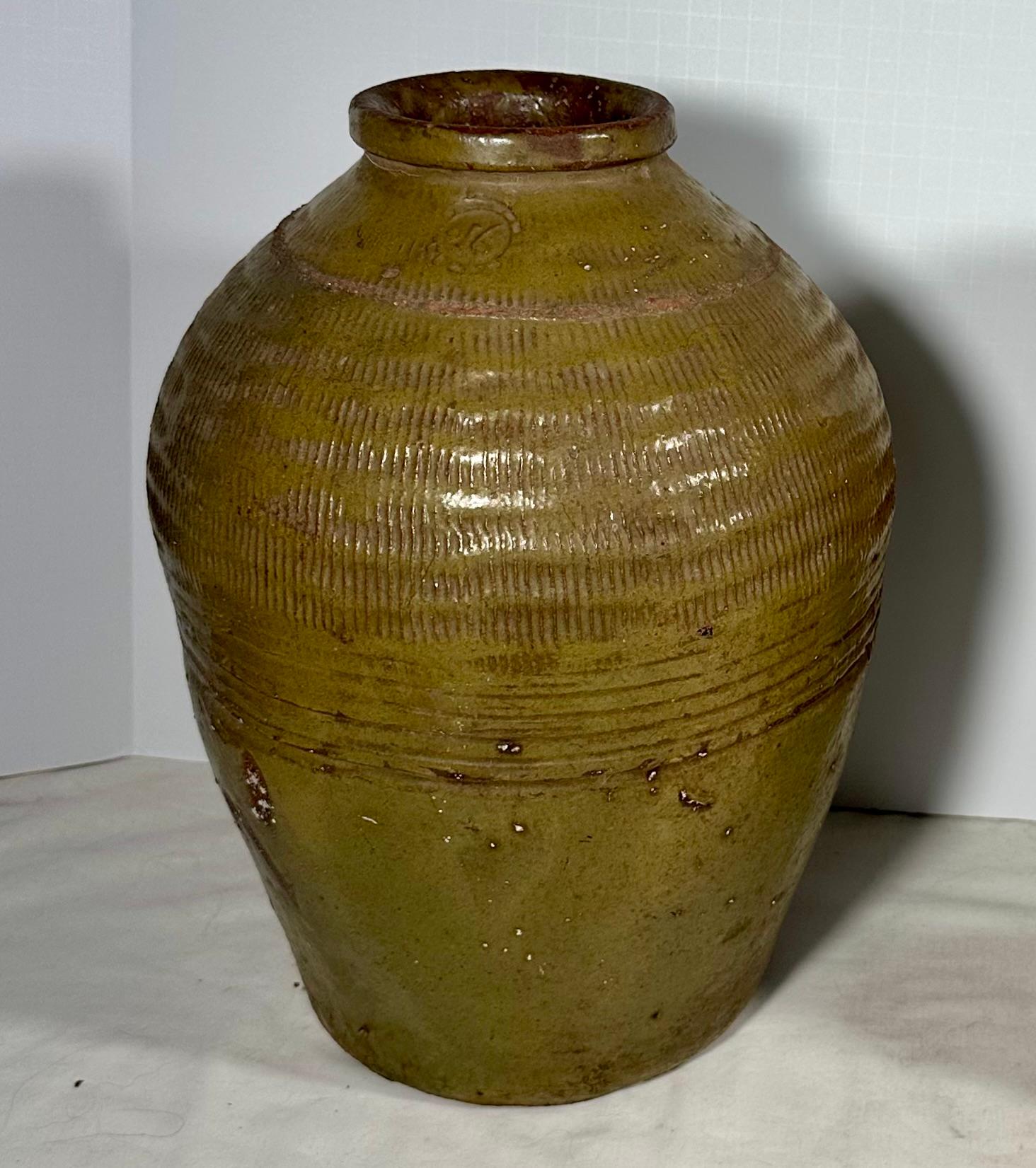 Pair 19th Century Chinese Glazed Pickling Jars.

Each of these glazed ceramic jars have small, hemmed openings, linear striations pressed in the upper shoulders and a circular stamp. The surface of each is glazed in an olive green color.  The jars
