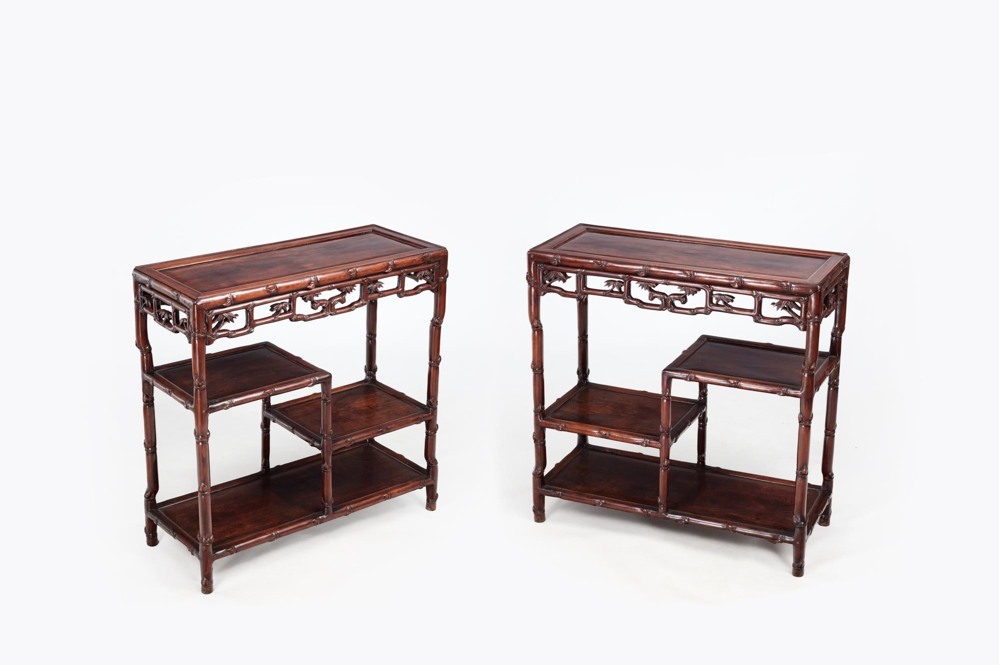 Pair of 19th Century Chinese Hong mu hardwood side tables featuring stepped display shelves. The panel tops above recessed friezes and aprons, raised on handcarved legs ending in shaped feet. The pair showcase richly textured, decorative handcarved