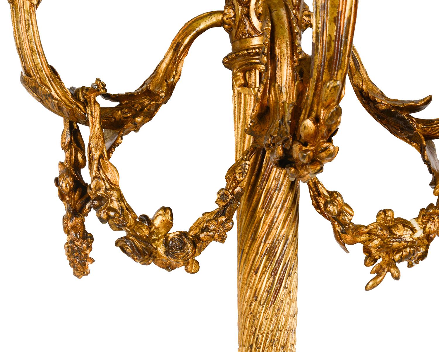 A classical pair of gilded ormolu Louis XVI style three branch wall lights, each with ribbons, arrow sheaths and scrolling foliate swags and decoration. Measures: 76cm (30
