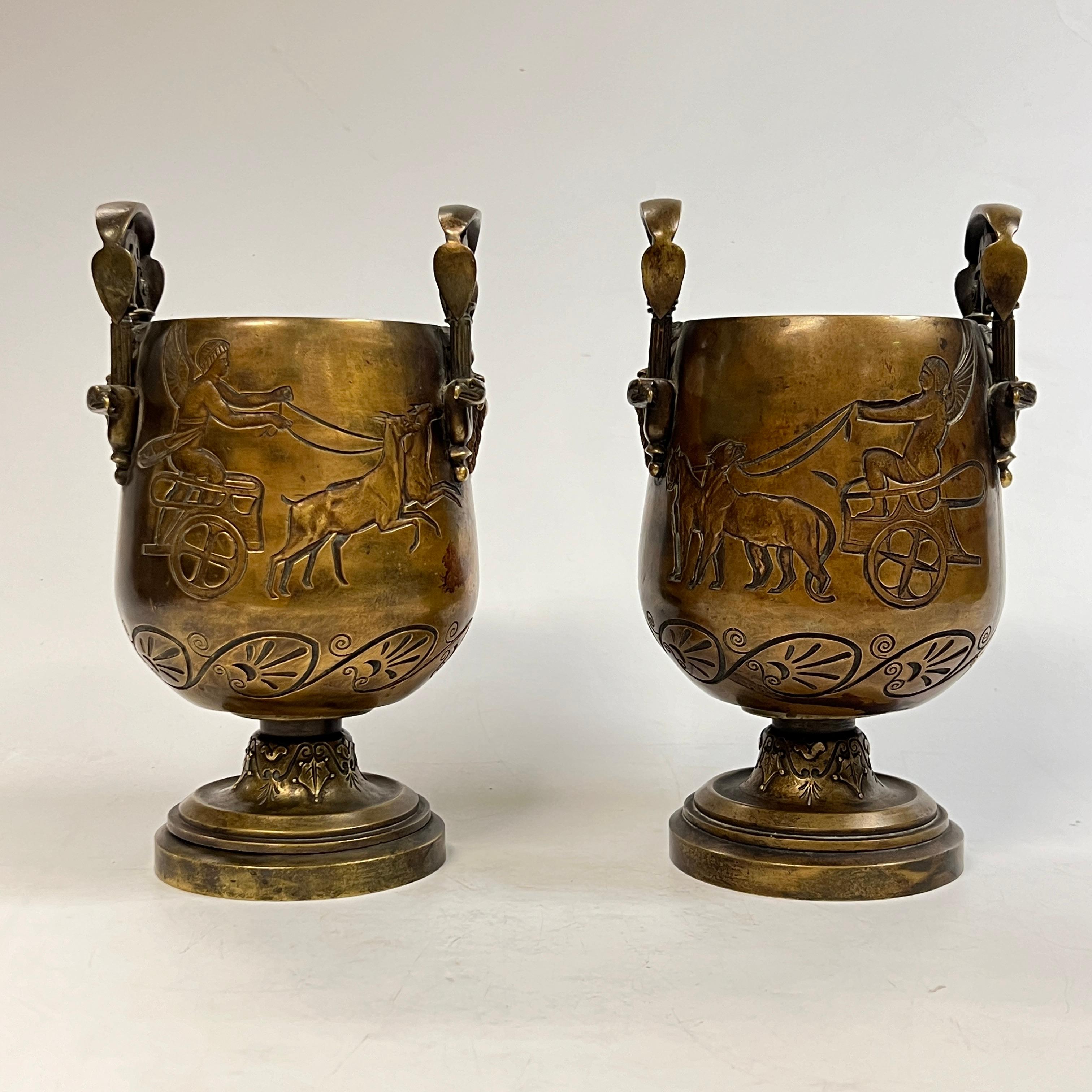 Coppia di vasi antichi (XIX secolo) in bronzo del periodo del Rinascimento egiziano raffiguranti carri trainati da leopardi su un lato e carri guidati da cervi sul lato opposto con manici raffiguranti maschere maschili e teste d'aquila. 