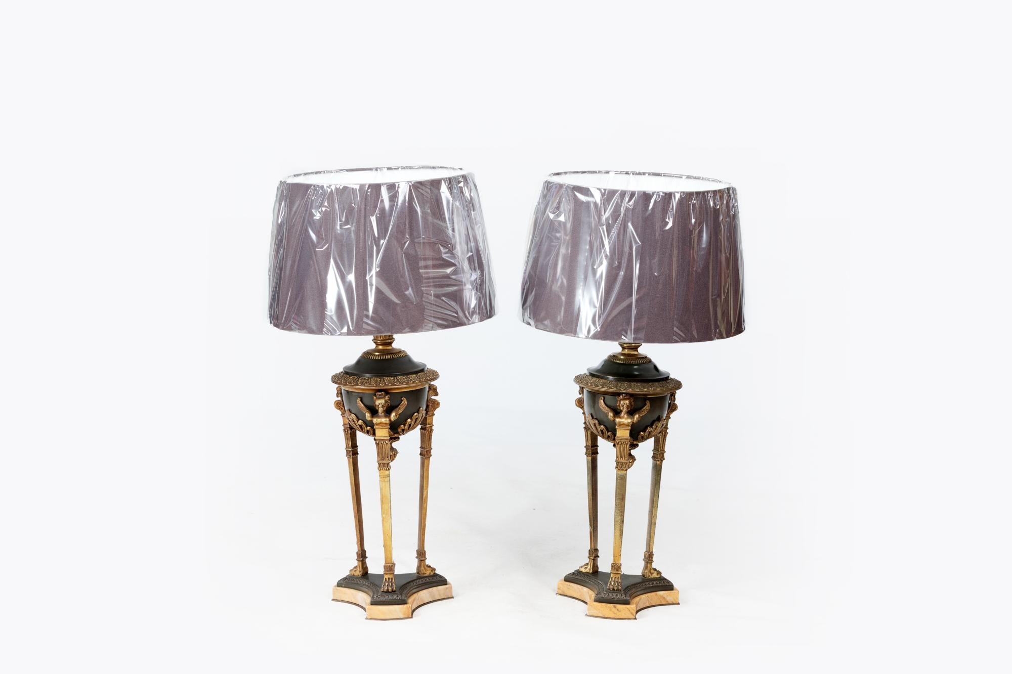 Pair of 19th Century Empire table lamps with three brass legs, ormolu eagle busts in relief and Corinthian style capitals. The pair sit on triform bases featuring lion paw feet on sienna marble plinths.