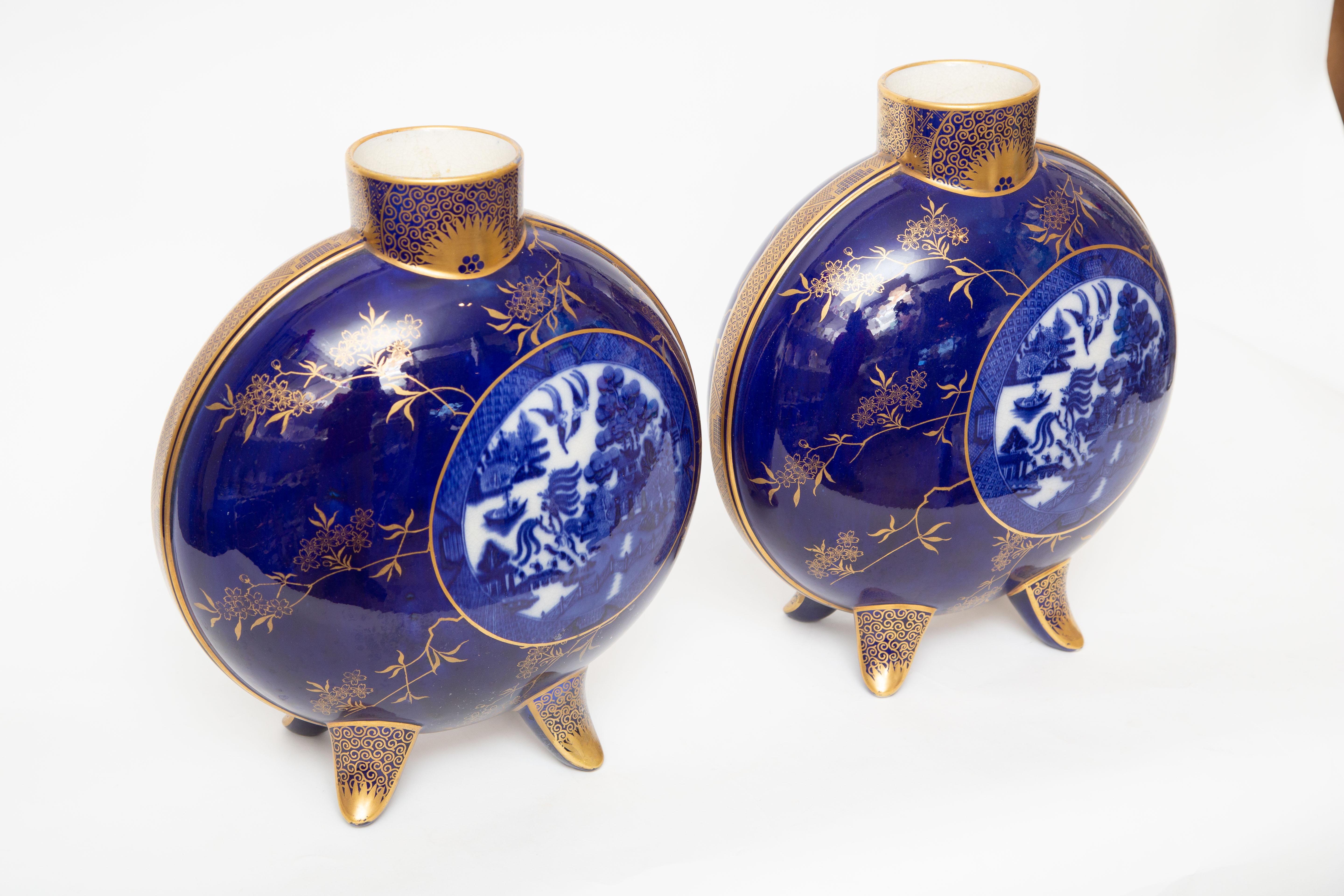 A finely decorated pair of deep rich blue vases with cartouches of the iconic Blue Willow pattern on their flow blue grounds. With adorable feet on their bases and moon shaped vessels they present a pleasing aesthetic. Rare and hard to find with in