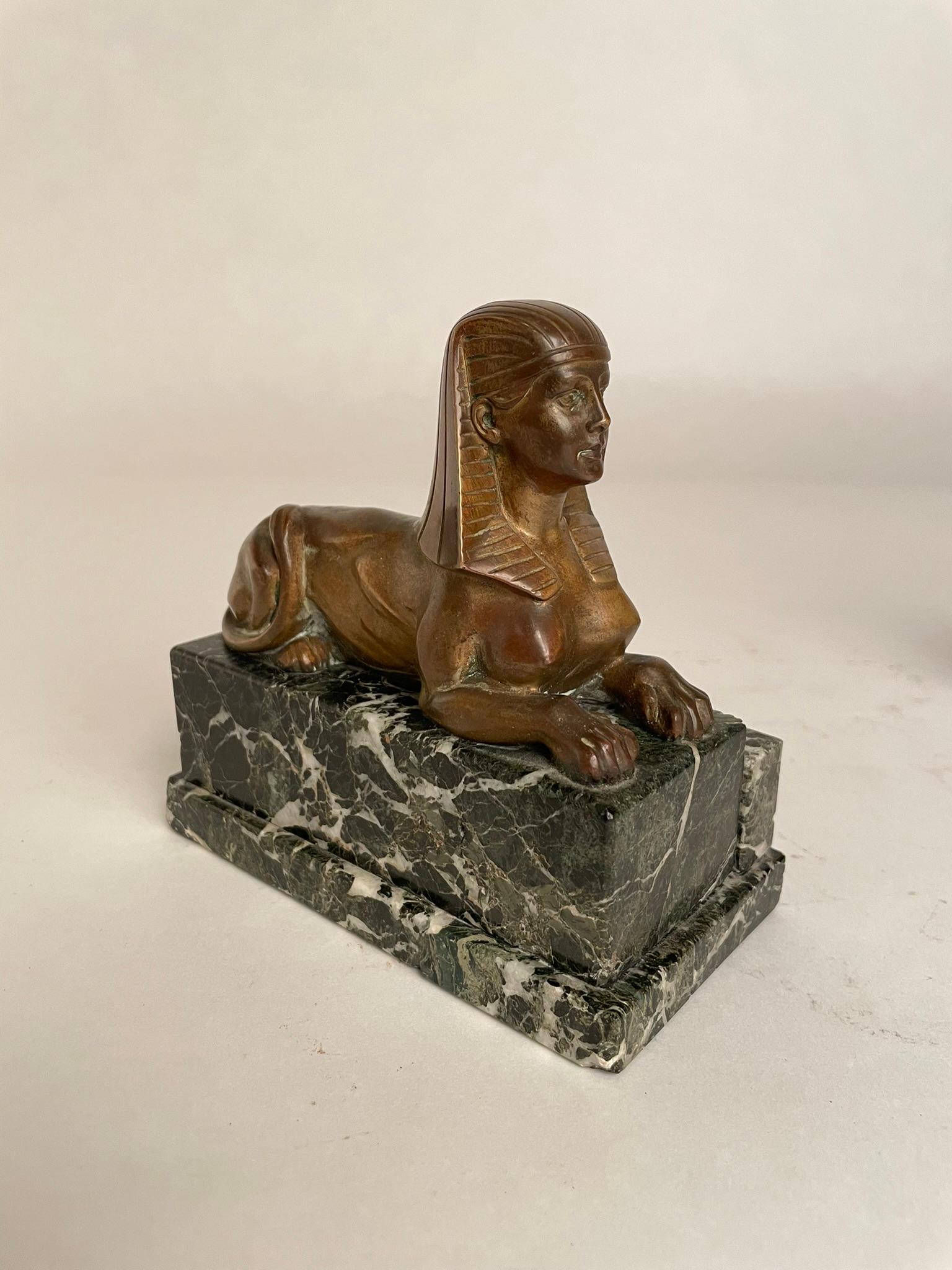 A pair of French Empire bronze models of recumbent Sphinxes on Verdi Antico marble bases. The bronze with the warm golden patina of age. The custom marble bases, stepped on one side were likely made to be used as book ends. These make a handsome
