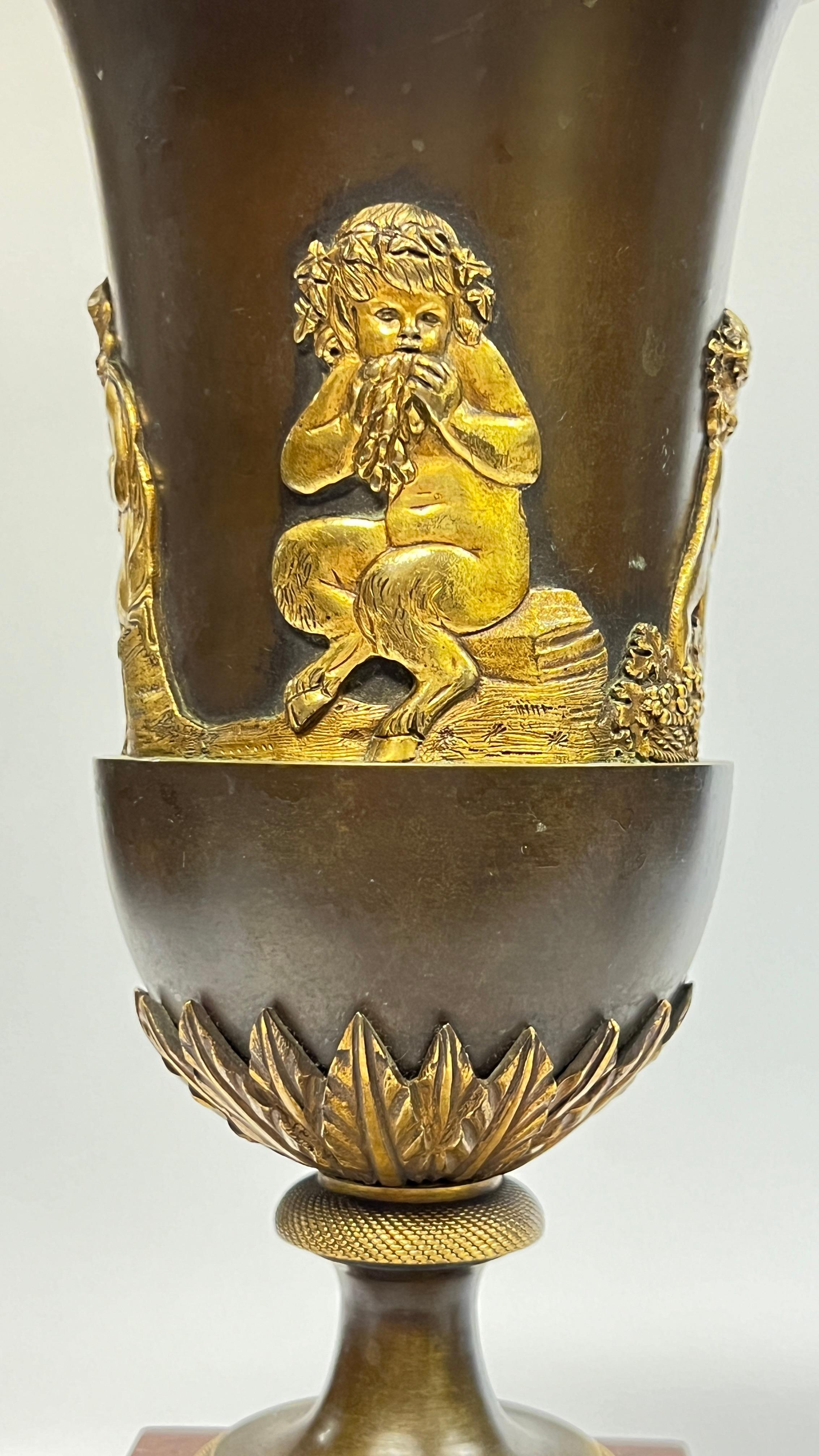 Coppia di antichi vasi a campana in bronzo dorato del periodo Impero francese, ciascuno di 13 3/4 per 6 7/8 pollici, 1810 circa, con collo svasato con bordo in bronzo dorato, decorato con putti e fauni bacchici e foglie d'acanto, montati su plinti