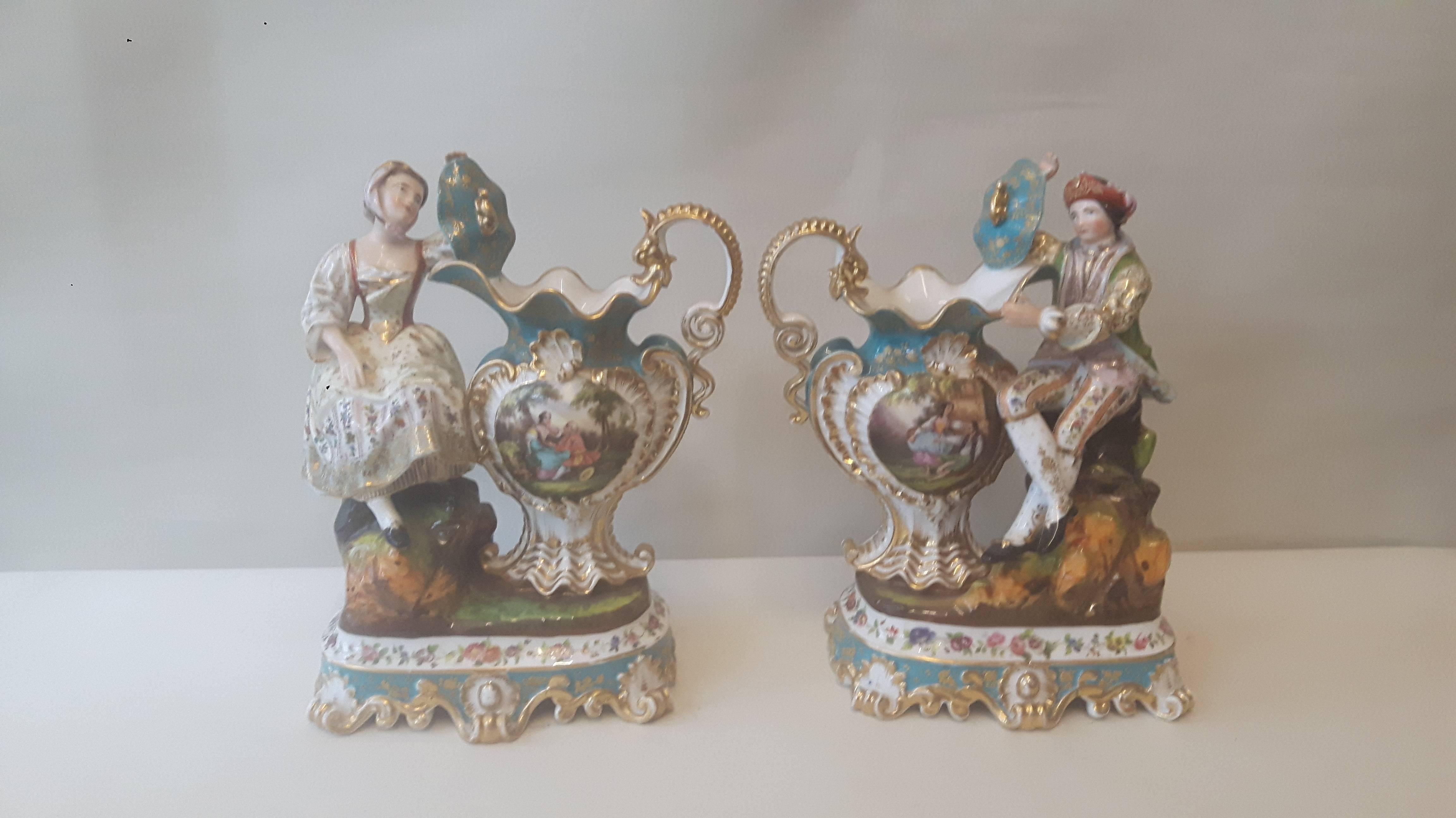 A very unusual pair of figurines of a lady and her beau in C18 dress by Jacob Petit, sitting besides an elaborately decorated urn with hand-painted cartouches after Watteau. Each urn has an intricate gilded handle in the shape of a dragon and the
