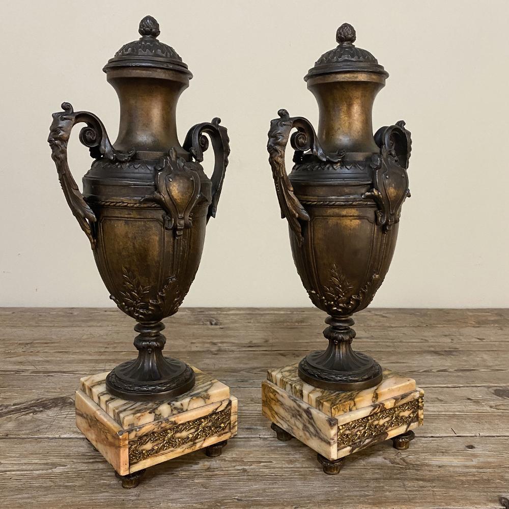 Pair of 19th century French Louis XVI mantel urns on marble bases were intended for decorative appeal alone, and feature classic designs inspired by ancient Greek amphora and Romanesque architectural embellishment. Cast from spelter, each has been