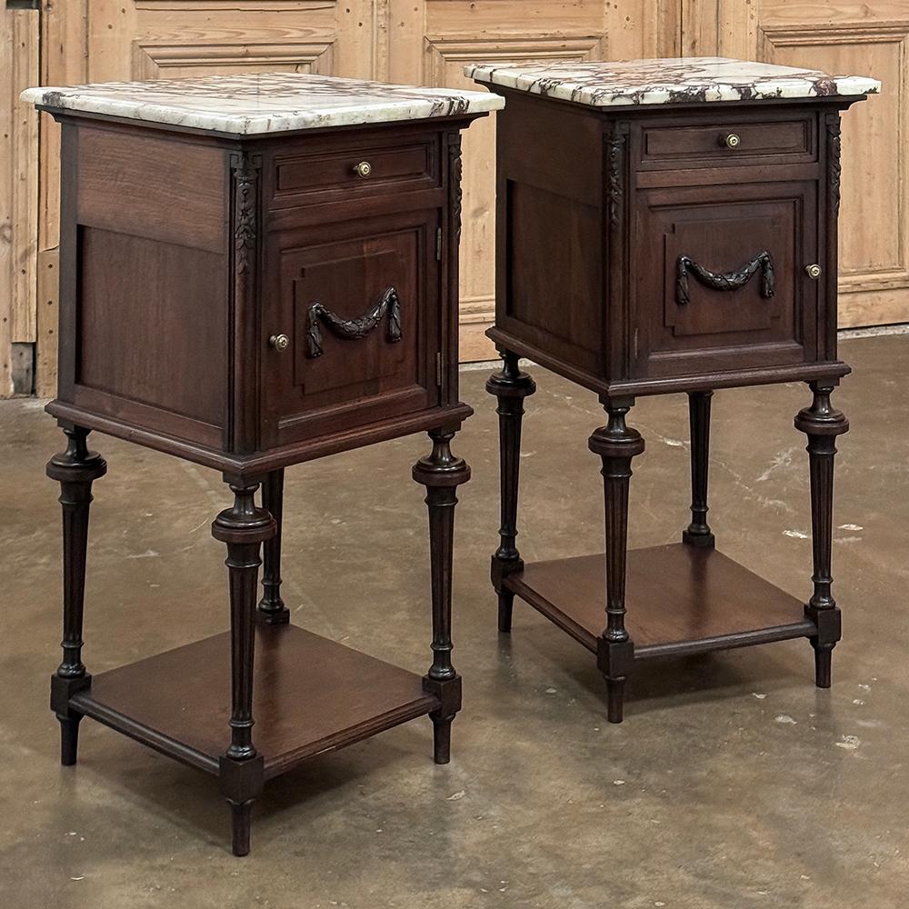 Pair 19th Century French Louis XVI Marble Top Nightstands were crafted in the traditional manner from fine walnut, the fitted with a bronze mount depicting a laurel swag on each door, and cast brass knobs to open each drawer and cabinet door.  Fine