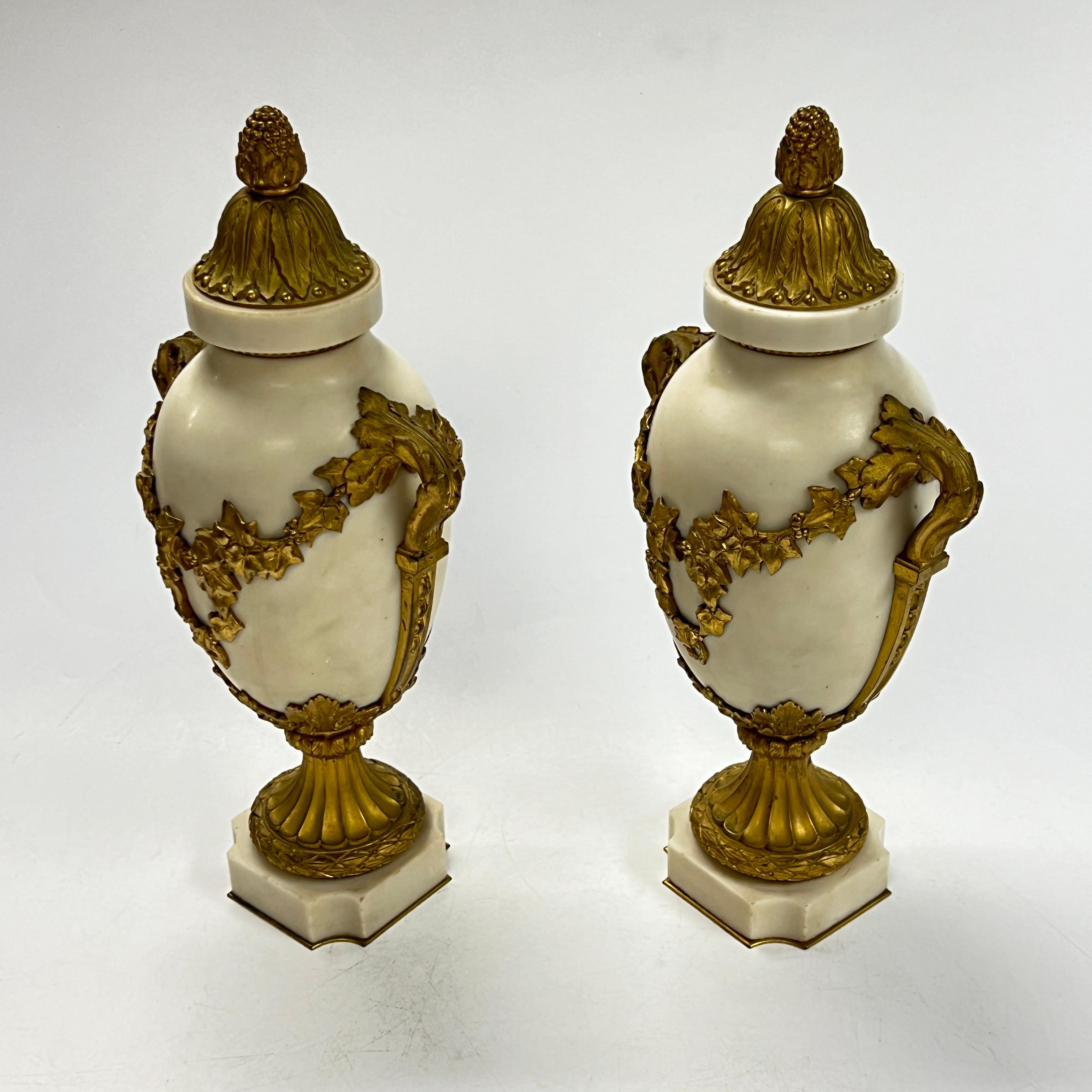 Coppia di belle urne antiche (fine del XIX secolo) in stile Luigi XVI, realizzate in marmo bianco con montature in bronzo dorato con motivi neoclassici, tra cui volute floreali, bacche e foglie d'acanto.