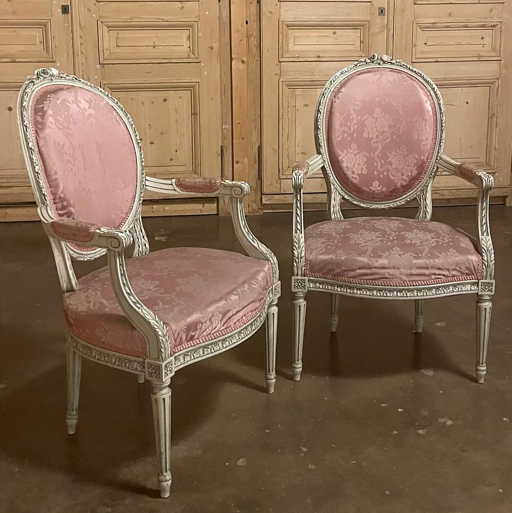 Pair 19th century French Louis XVI painted armchairs is a superlative decorative accent that just happens to provide seating! Hand-carved from solid walnut, each features a distinctive neoclassical theme in its carved embellishment that is enhanced