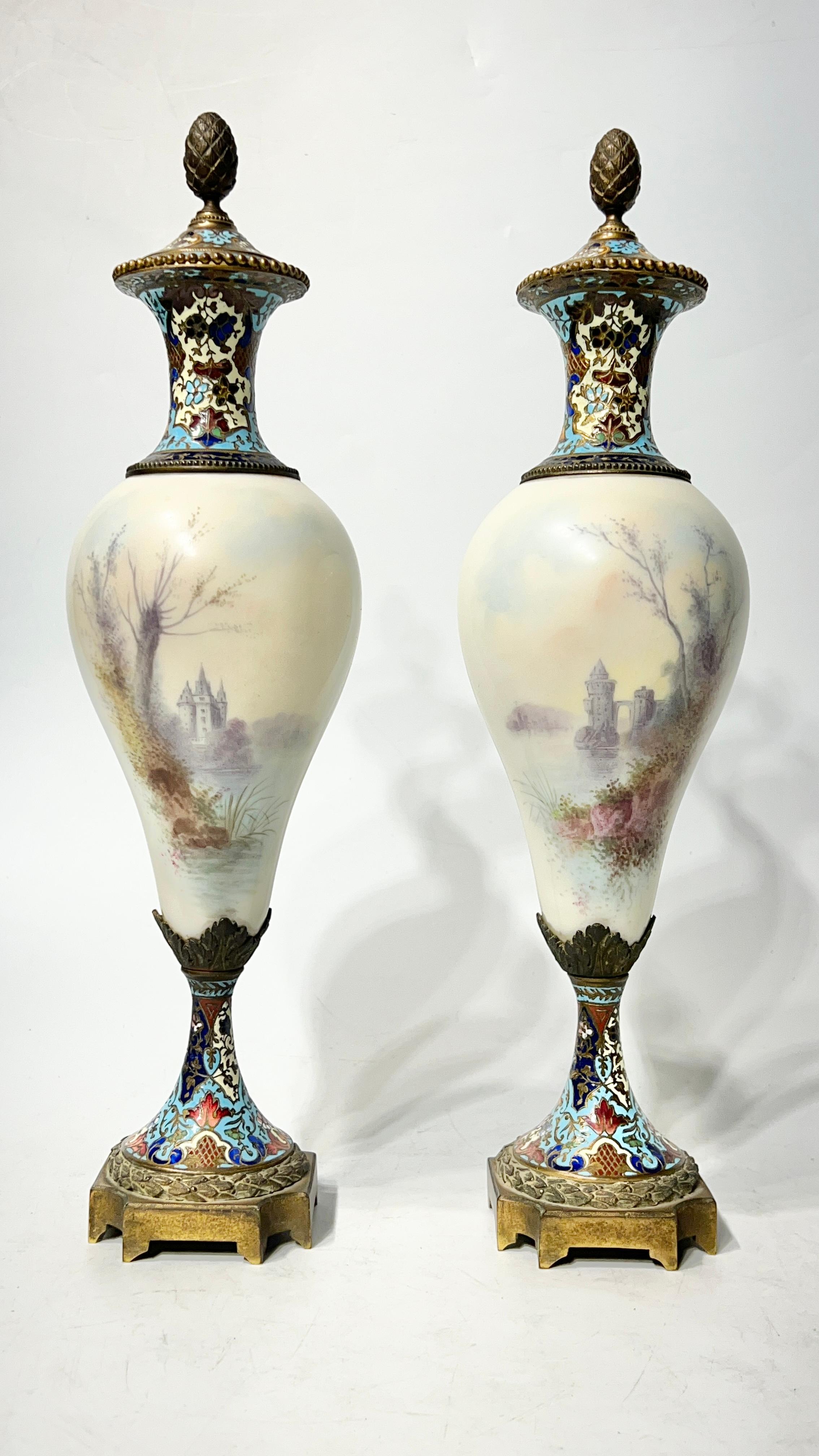 Pair of antique (late 19th century) French porcelain vases with covers, distinguished by their champleve enamel inlaid bronze mounts, and lovely figurative scenes of courting lovers on front and idyllic rural scenes of castles.  Each signed.