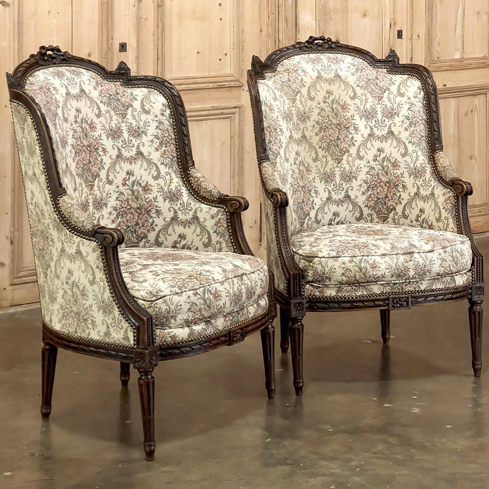 Pair 19th Century French Louis XVI Walnut Bergeres ~ Armchairs envelope one in comfort, and do it in classic style!  Crafted from sumptuous French walnut, the design features an arched seat back crown accented with a small floral wreath with ribbon