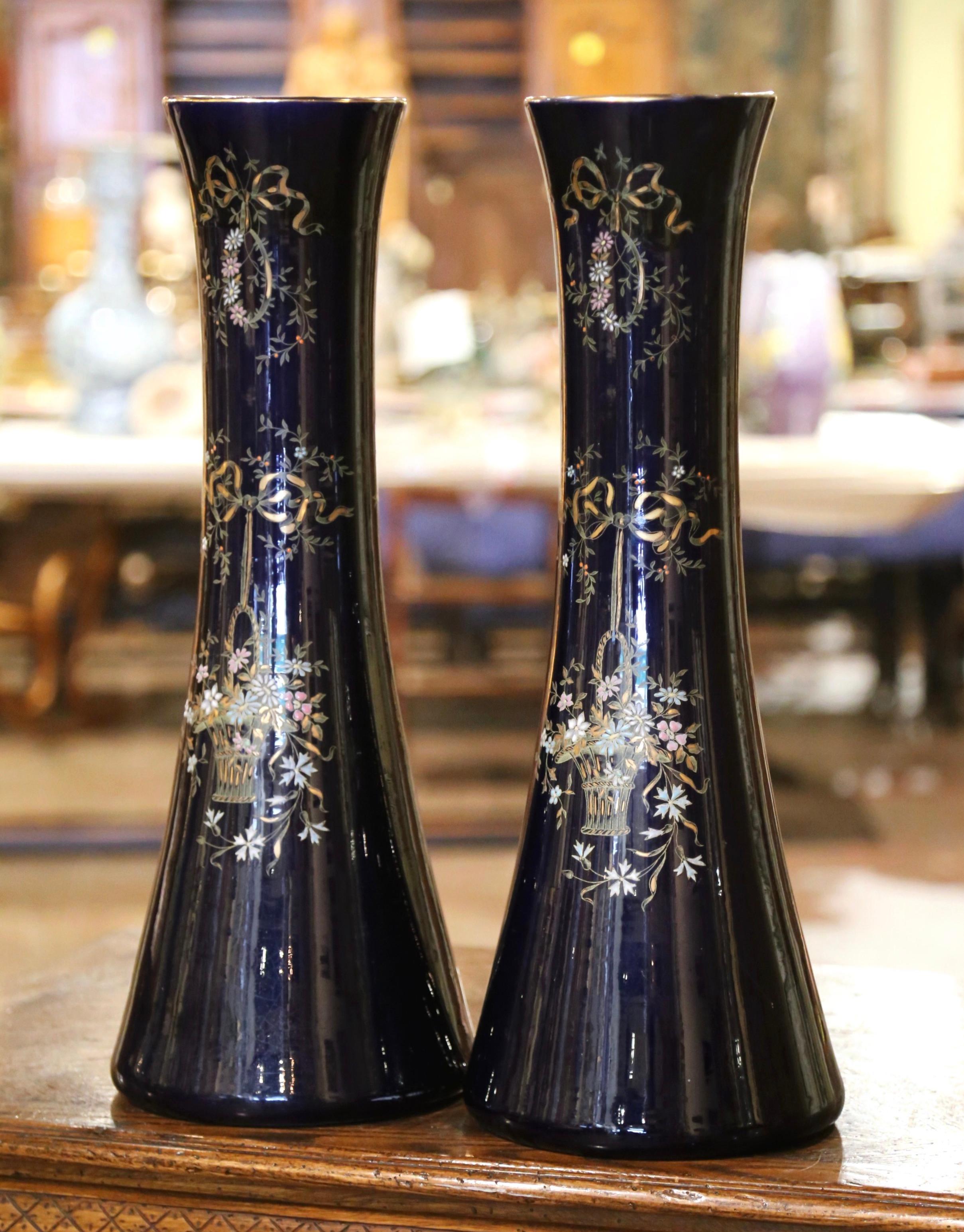 Decorate a console or a buffet with this elegant pair of antique vases from Paris. Crafted circa 1890, the tall neoclassical vessels feature a long, convex neck extending over a circular base. Each urn is gilt hand-painted with a several feminine